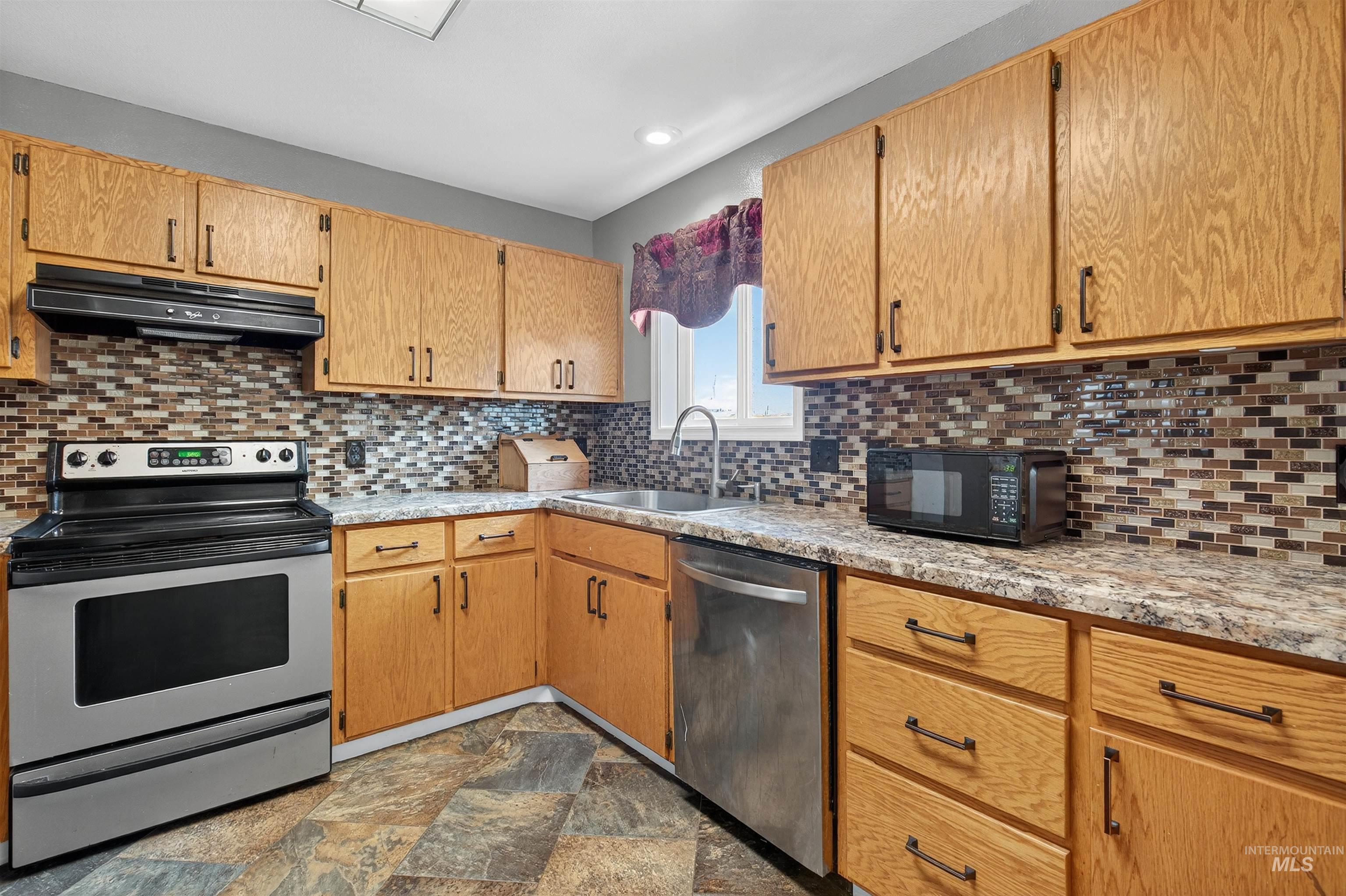 Kitchen featuring appliances with stainless steel finishes, tasteful backsplash, under cabinet range hood, stone finish floors, and recessed lighting