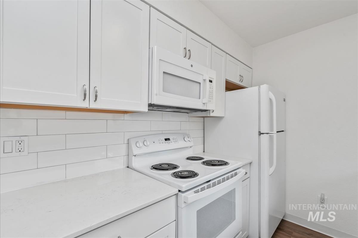 Kitchen with white appliances, backsplash, white cabinetry, and dark wood-style flooring