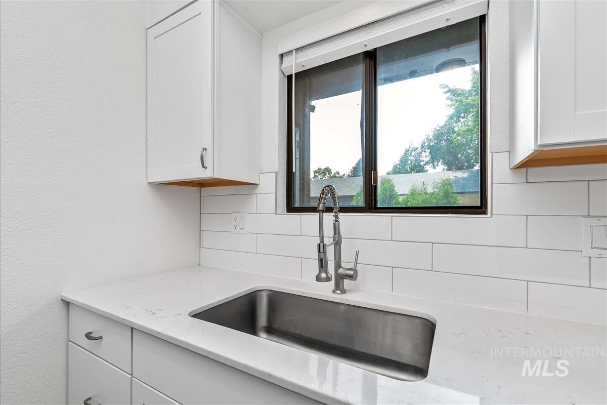 Kitchen with decorative backsplash, white cabinetry, and light stone counters