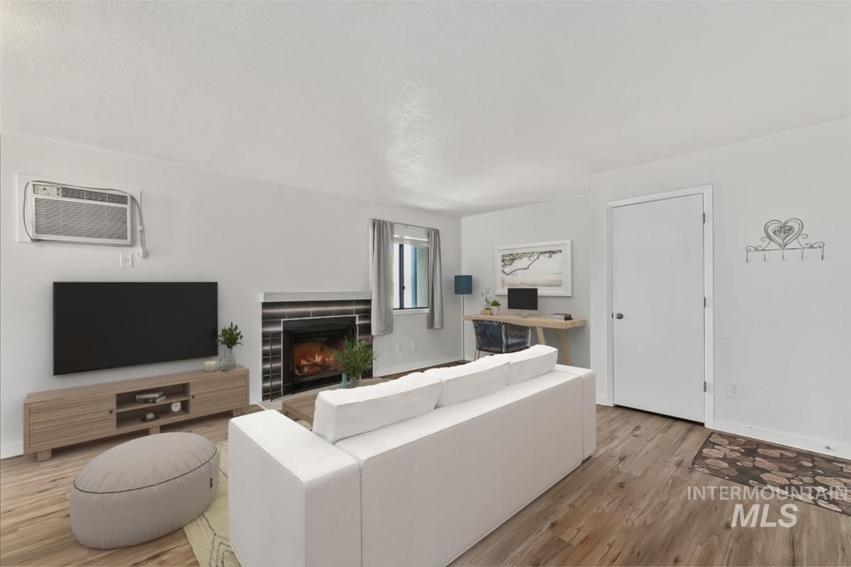 Living room featuring a fireplace, wood finished floors, and an AC wall unit