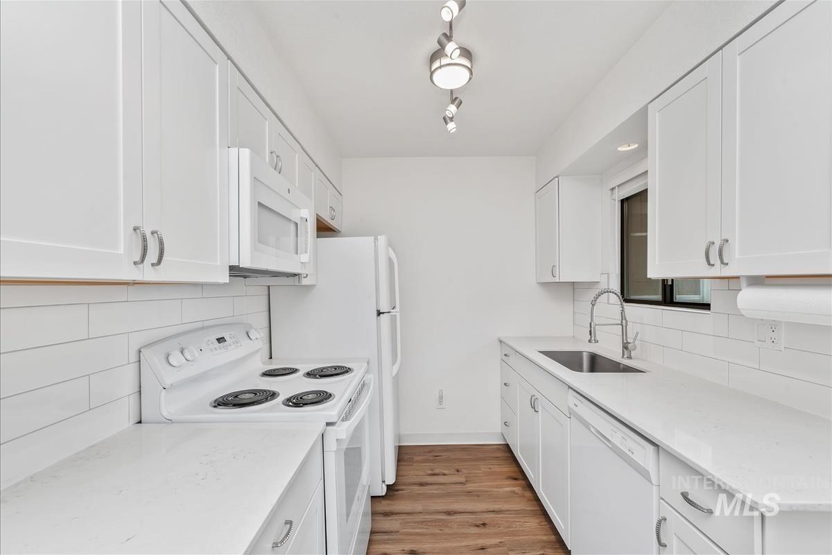 Kitchen with decorative backsplash, white appliances, and white cabinets