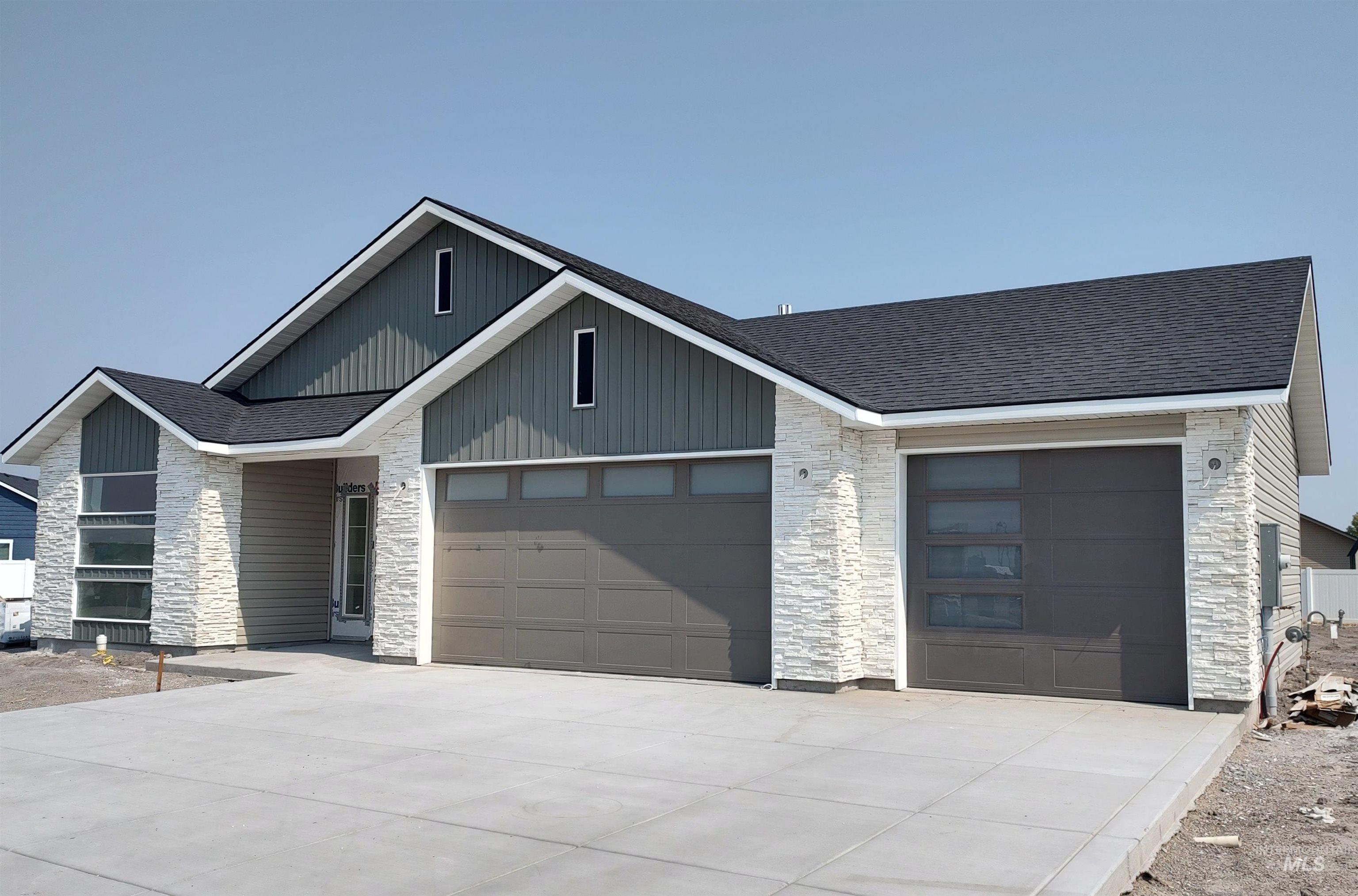 View of front of property featuring stone siding, roof with shingles, driveway, and a garage