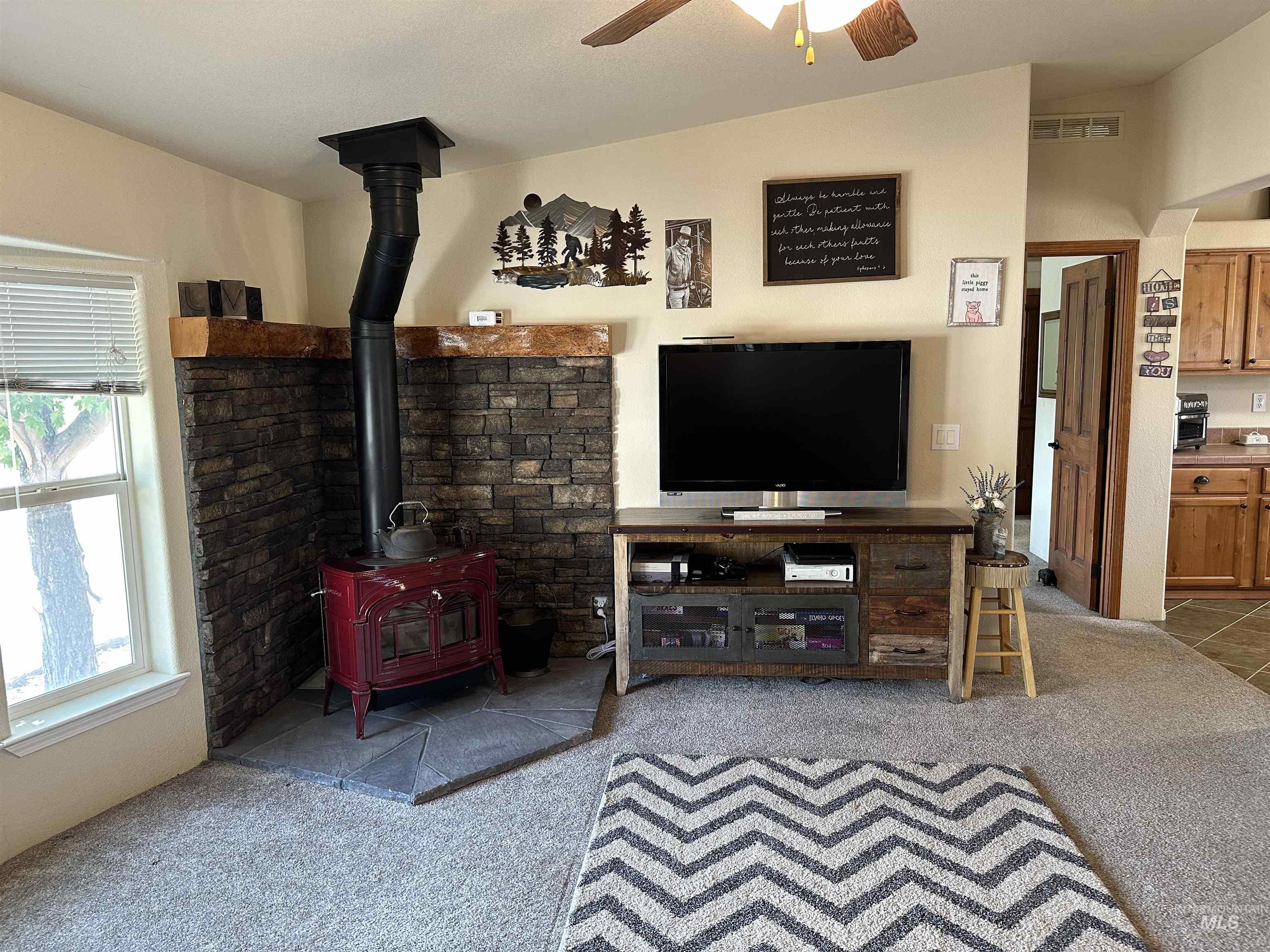 Living room featuring a wood stove, light colored carpet, and a ceiling fan