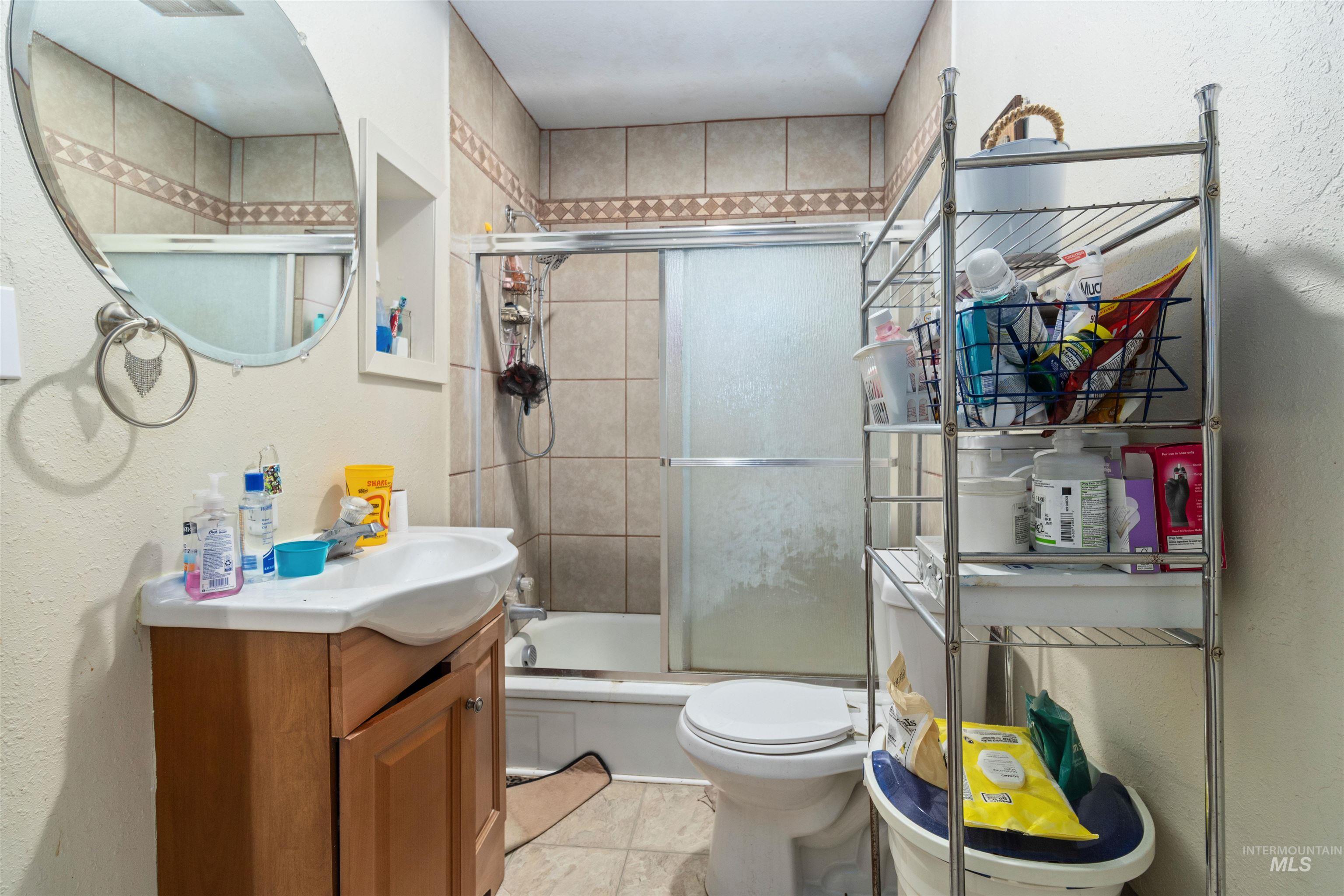Bathroom with a textured wall, combined bath / shower with glass door, vanity, and light tile patterned floors