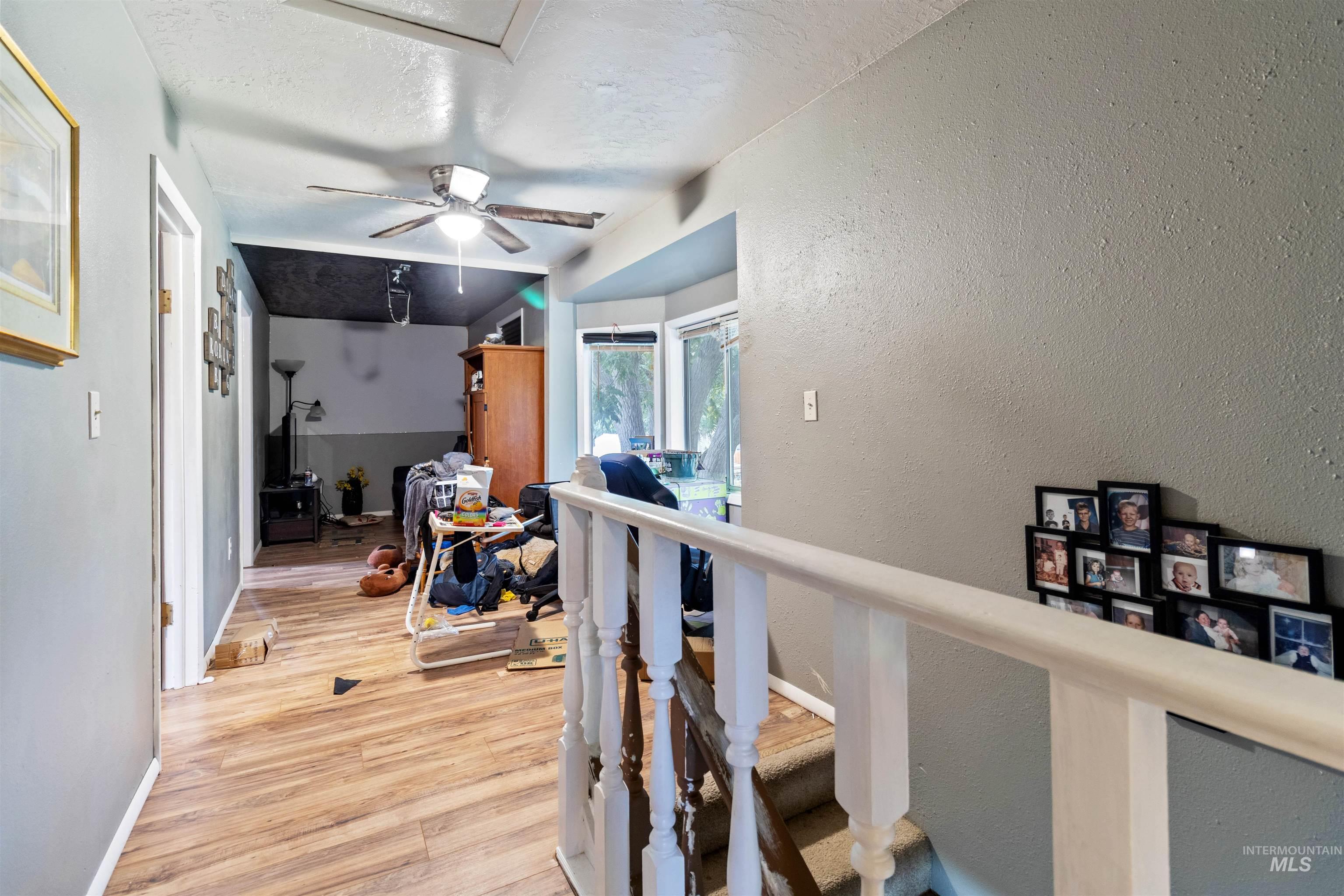 Hall featuring light wood finished floors, a textured wall, a textured ceiling, and an upstairs landing