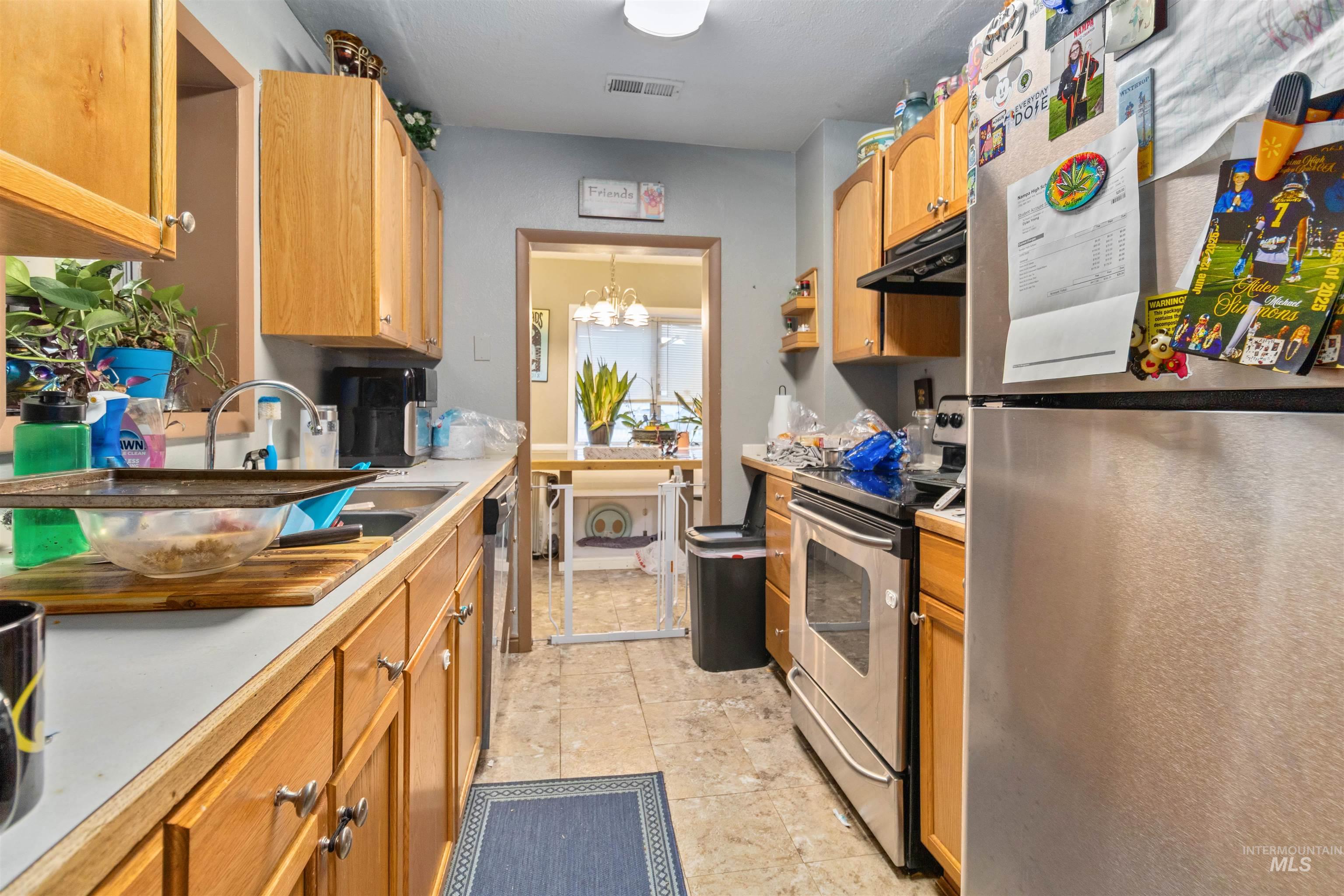 Kitchen with stainless steel appliances, under cabinet range hood, light countertops, a chandelier, and light tile patterned floors