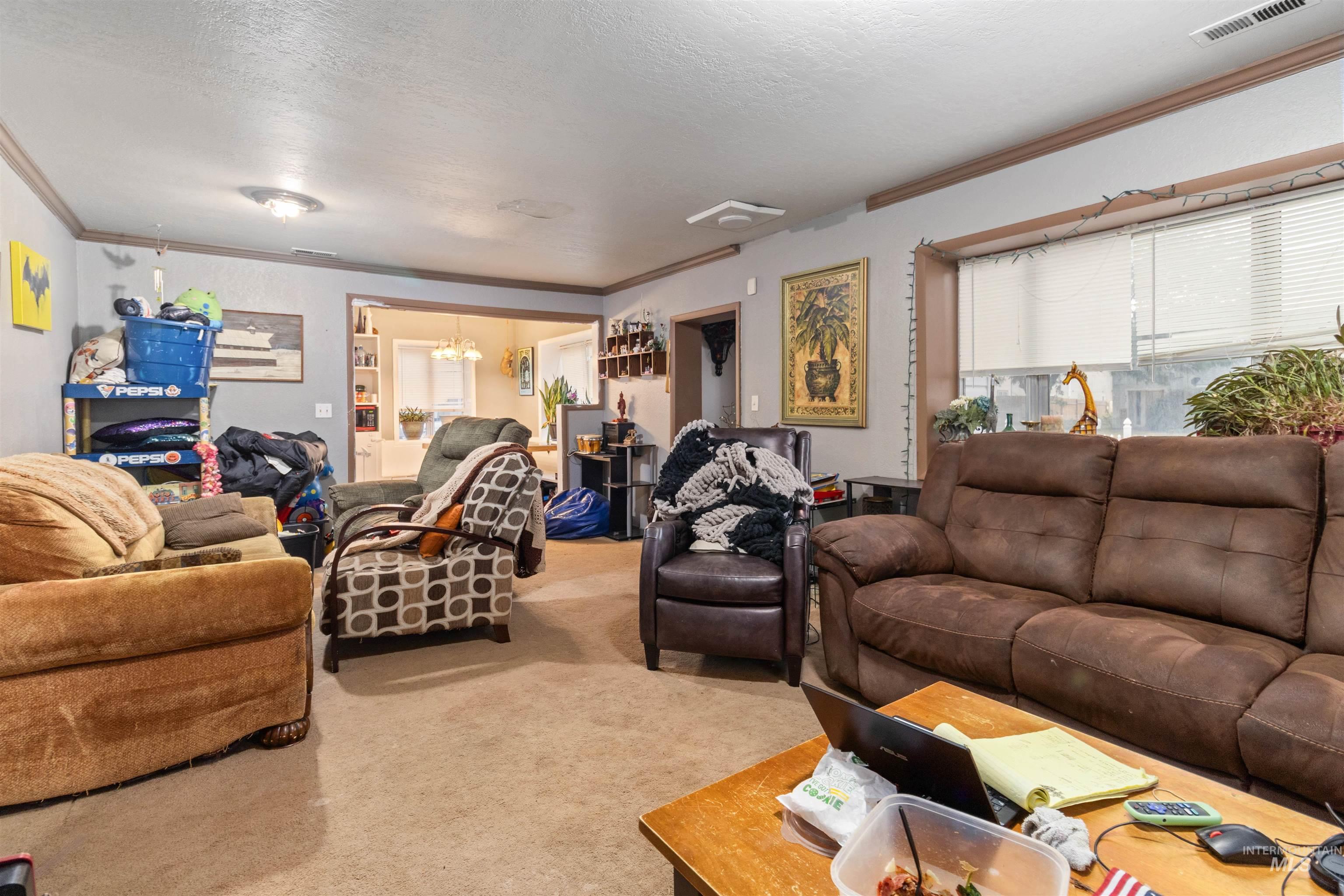 Carpeted living room with crown molding, a chandelier, and a textured ceiling
