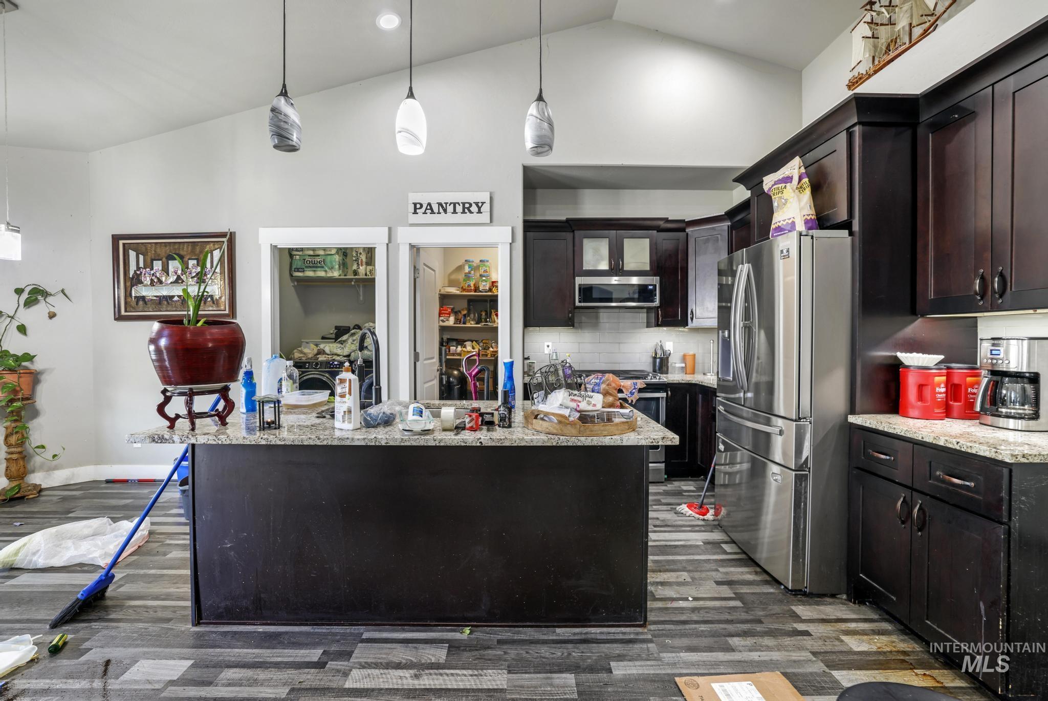 Kitchen with decorative backsplash, appliances with stainless steel finishes, pendant lighting, dark brown cabinetry, and light stone counters