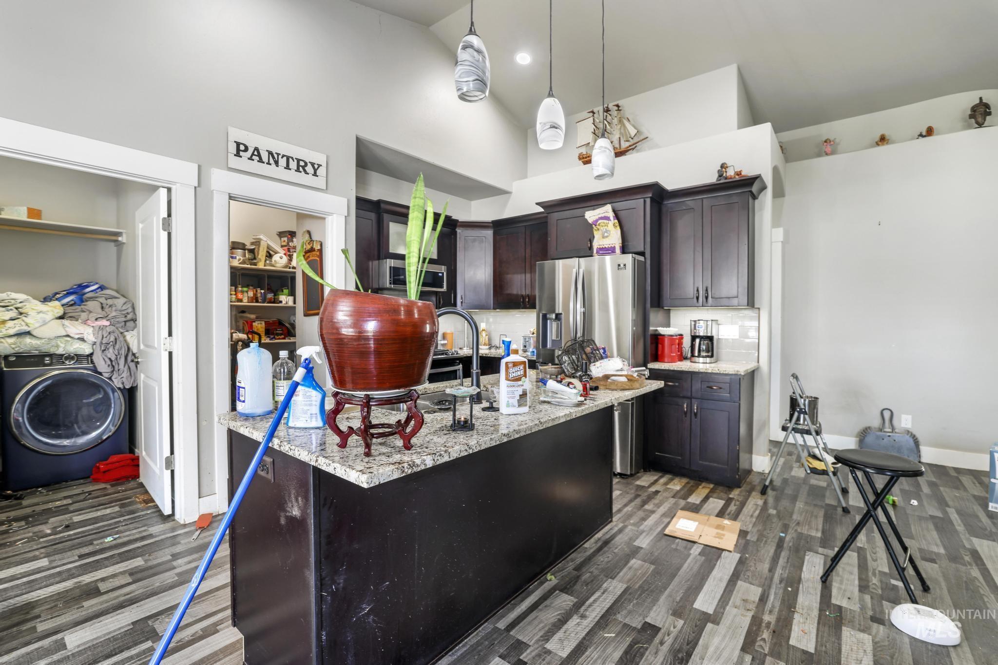 Kitchen featuring high vaulted ceiling, washer / dryer, light stone counters, pendant lighting, and dark brown cabinets