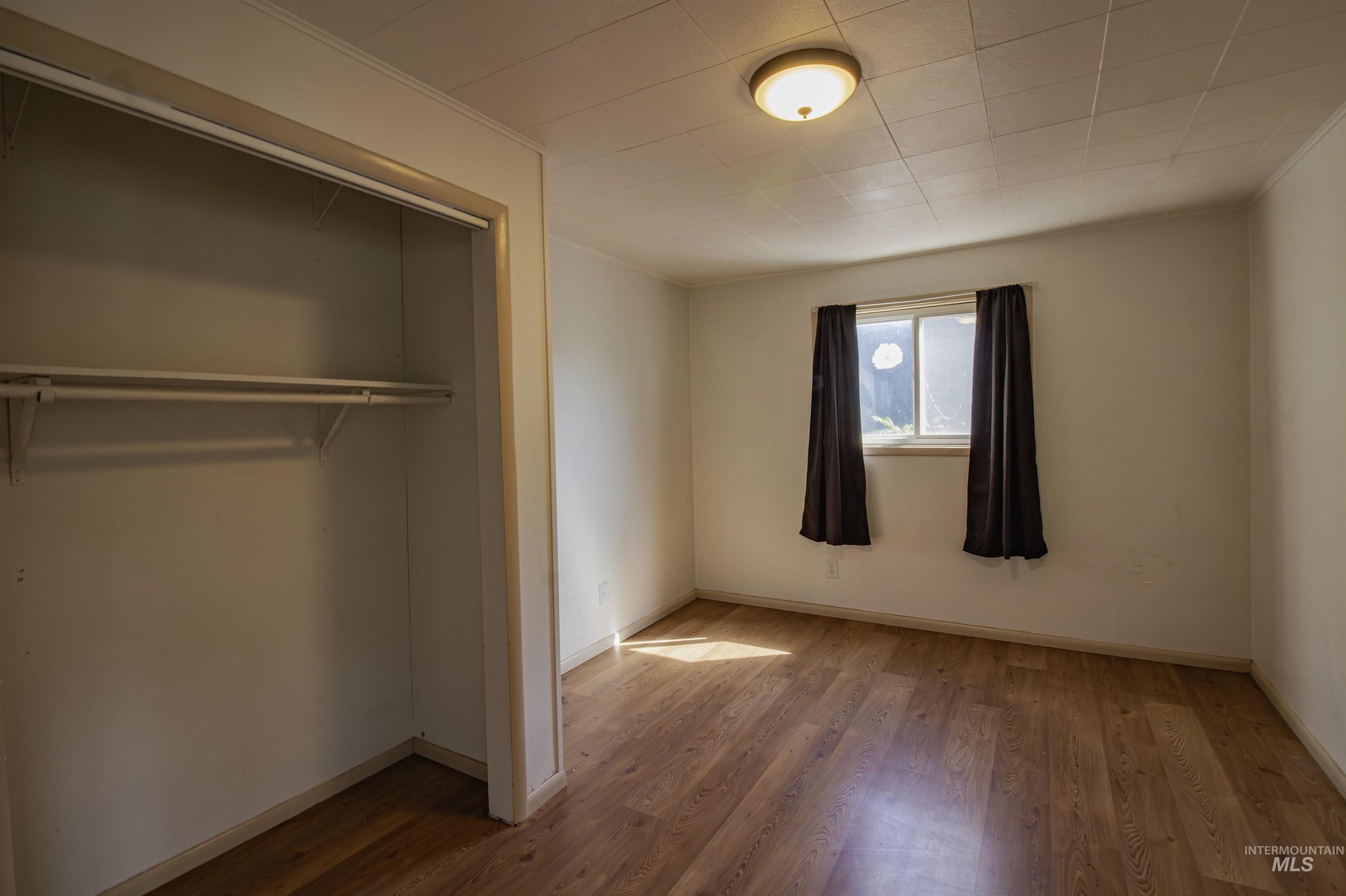 Unfurnished bedroom featuring wood finished floors, a closet, and ornamental molding