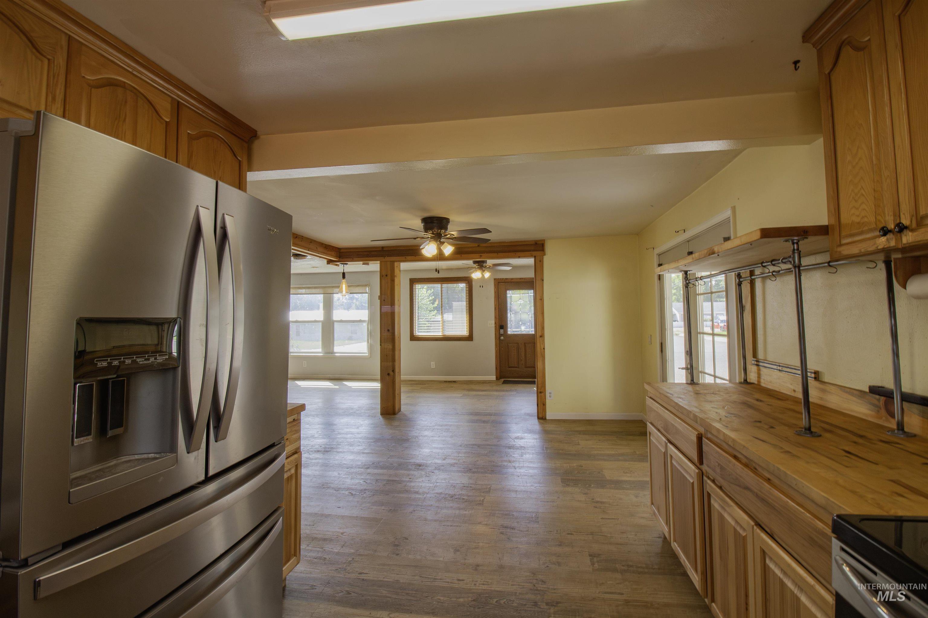 Kitchen with stainless steel refrigerator with ice dispenser, dark wood finished floors, a ceiling fan, range with electric stovetop, and brown cabinetry