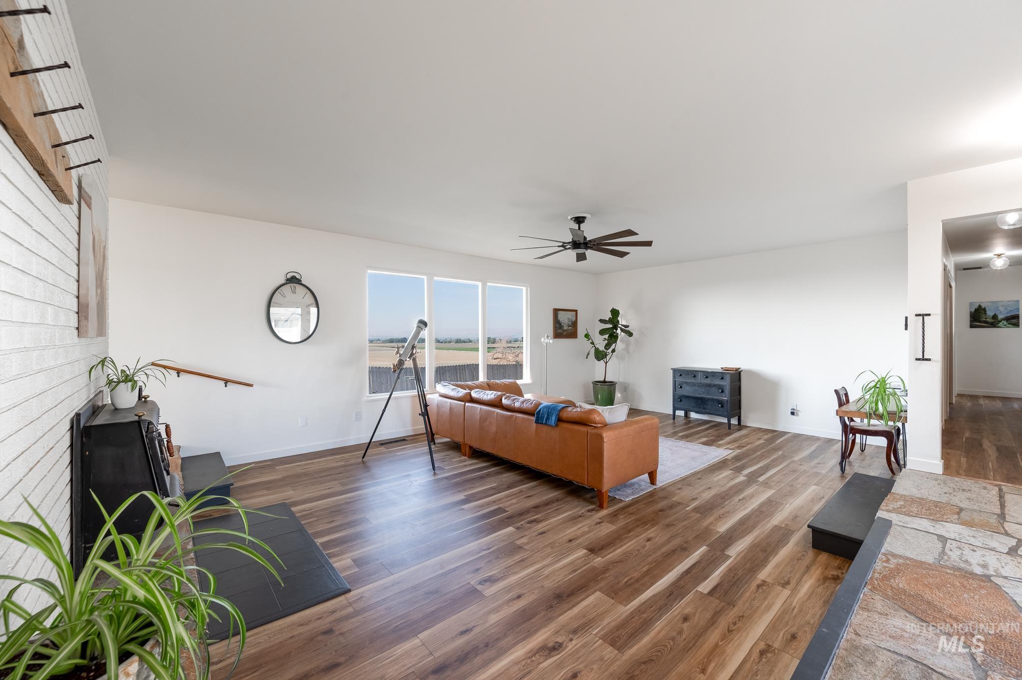 Living room featuring wood finished floors, ceiling fan, and a brick fireplace