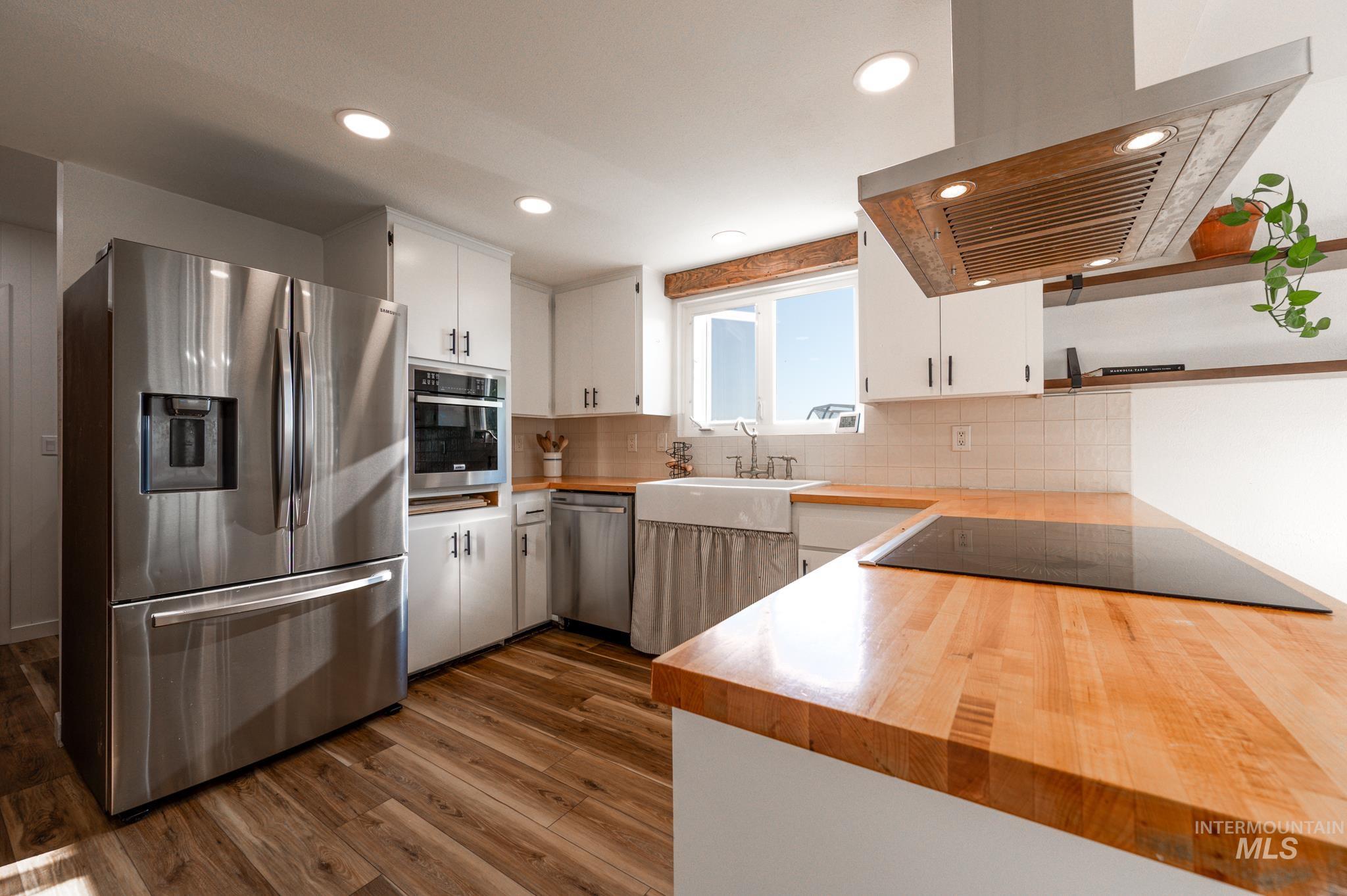Kitchen featuring white cabinets, stainless steel appliances, exhaust hood, dark wood-style floors, and tasteful backsplash