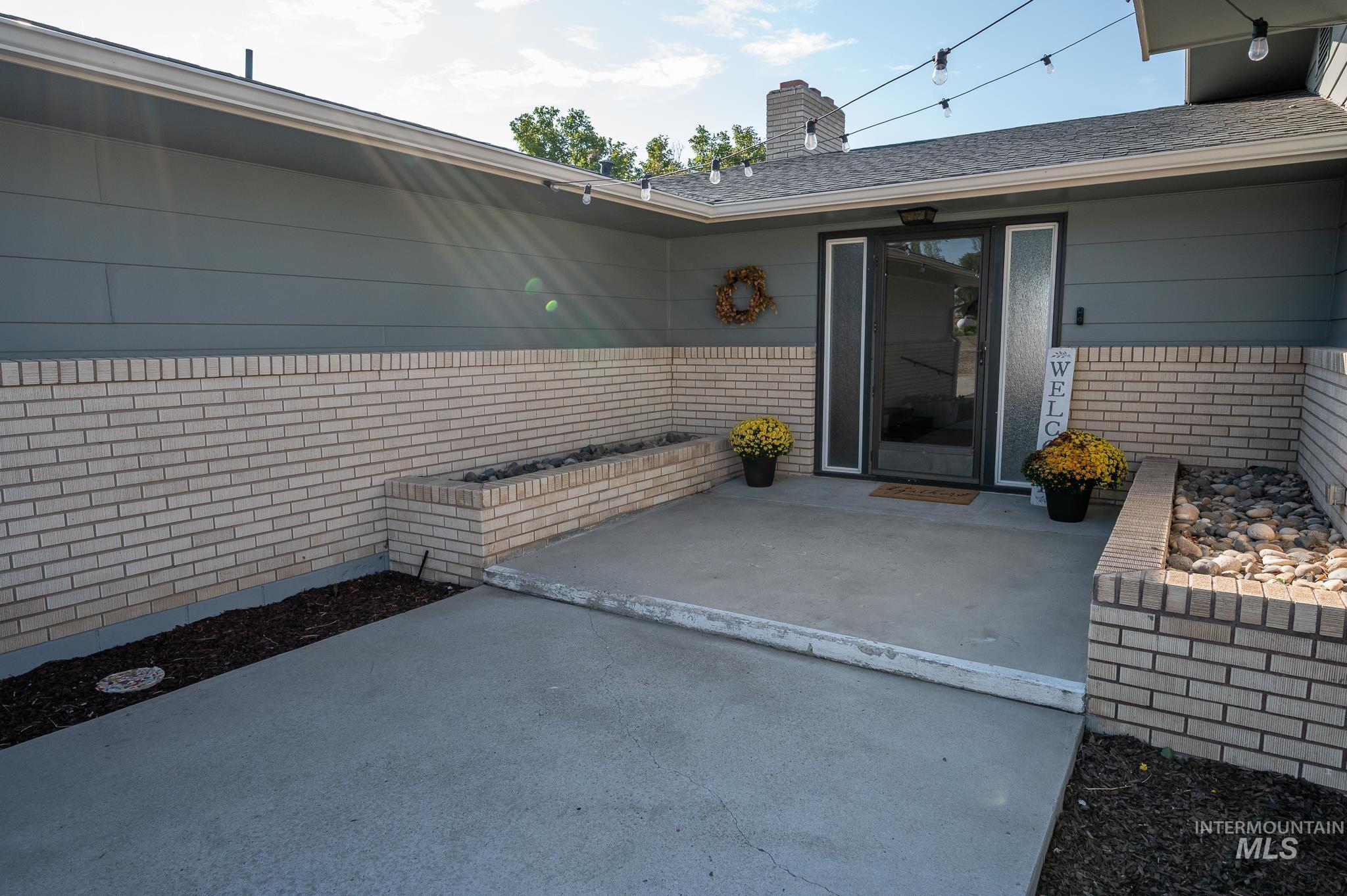 Entrance to property featuring a patio, brick siding, a chimney, and a shingled roof