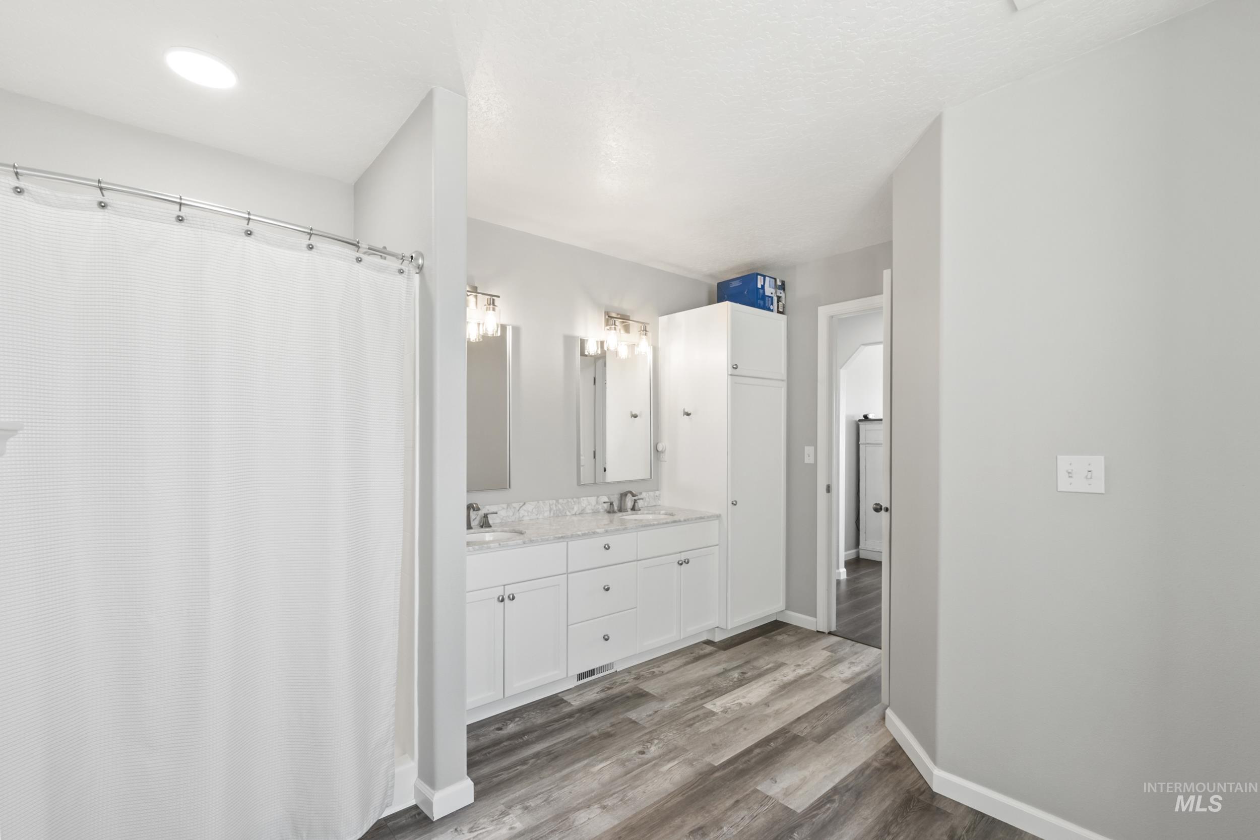 Full bath featuring double vanity, light wood finished floors, and curtained shower