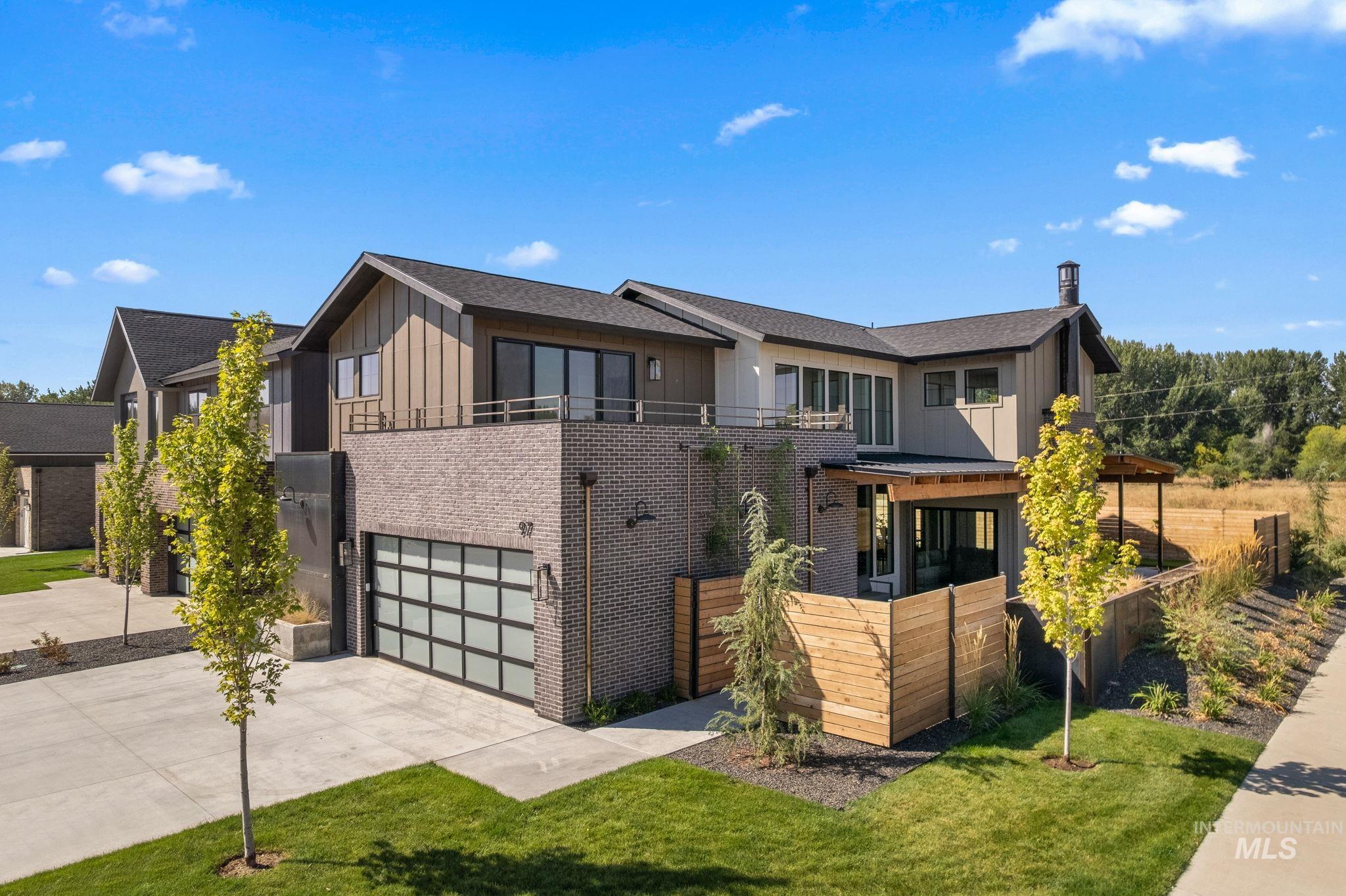 View of front of property featuring board and batten siding, brick siding, a garage, driveway, and a balcony