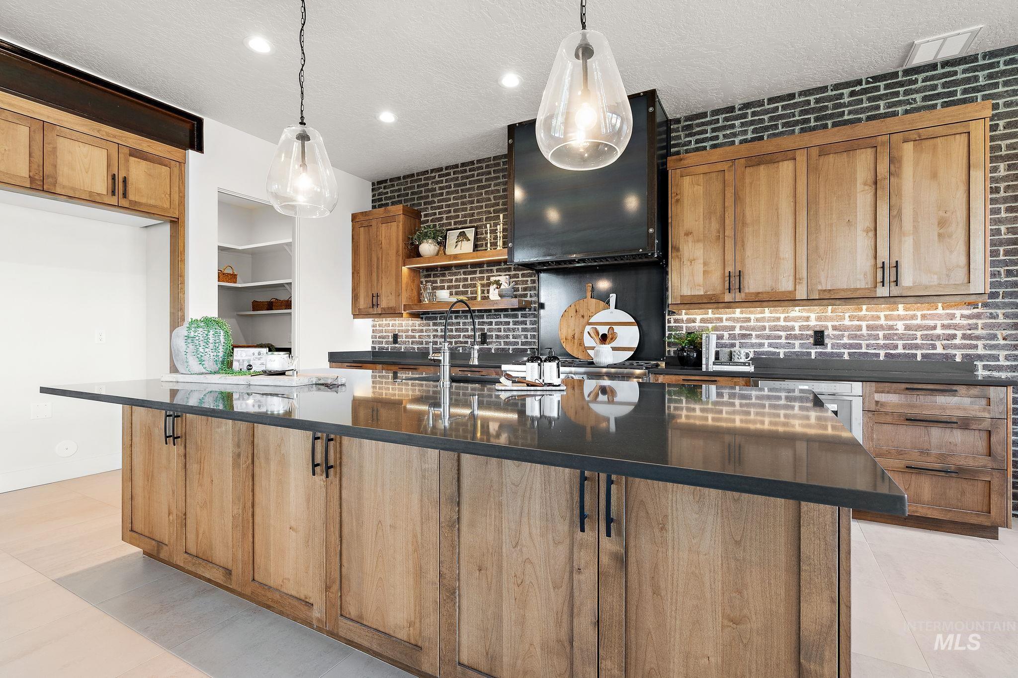 Kitchen featuring open shelves, a center island with sink, brown cabinetry, tasteful backsplash, and pendant lighting