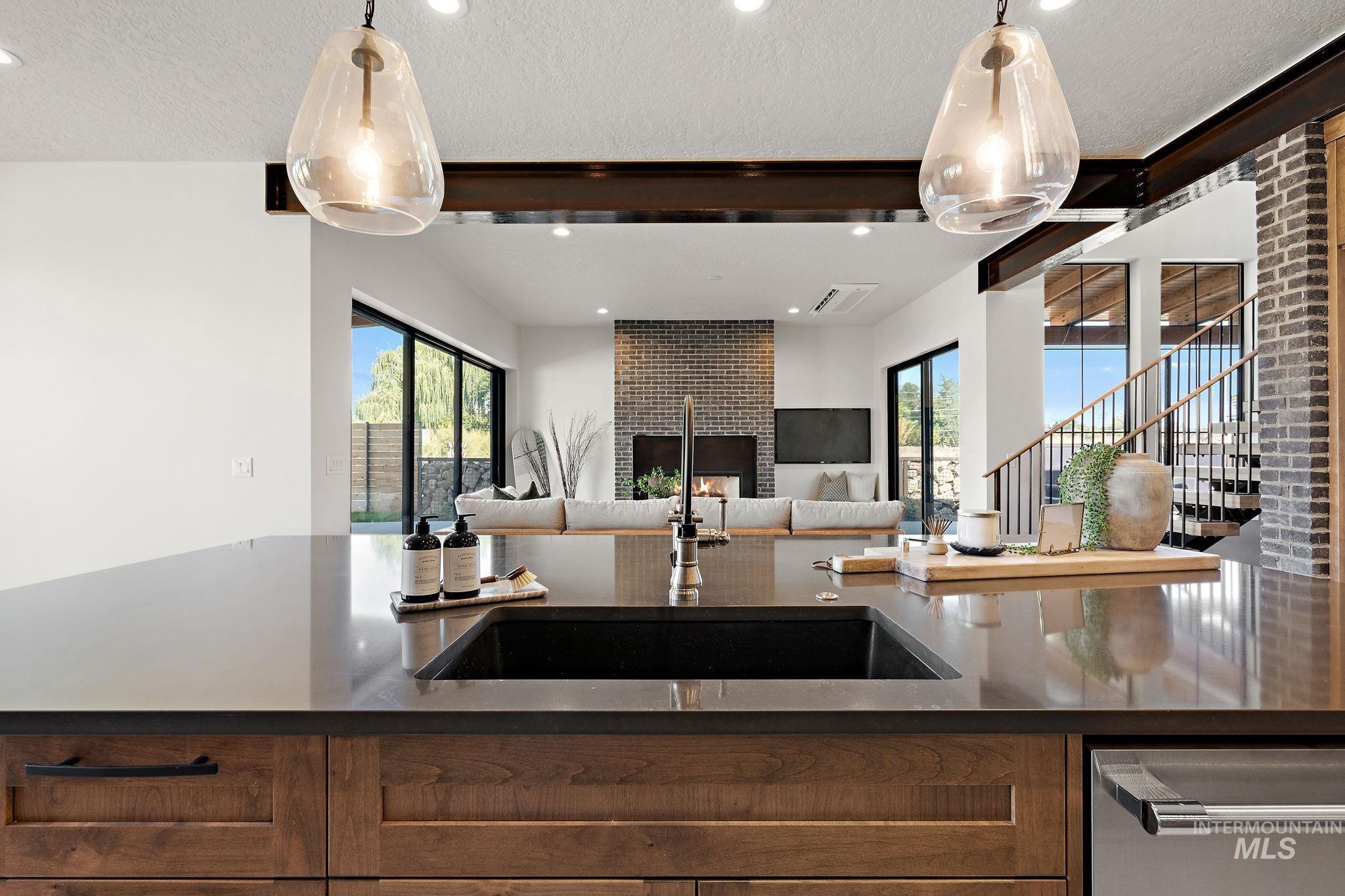 Kitchen with beamed ceiling, dark stone countertops, stainless steel dishwasher, brown cabinetry, and a textured ceiling