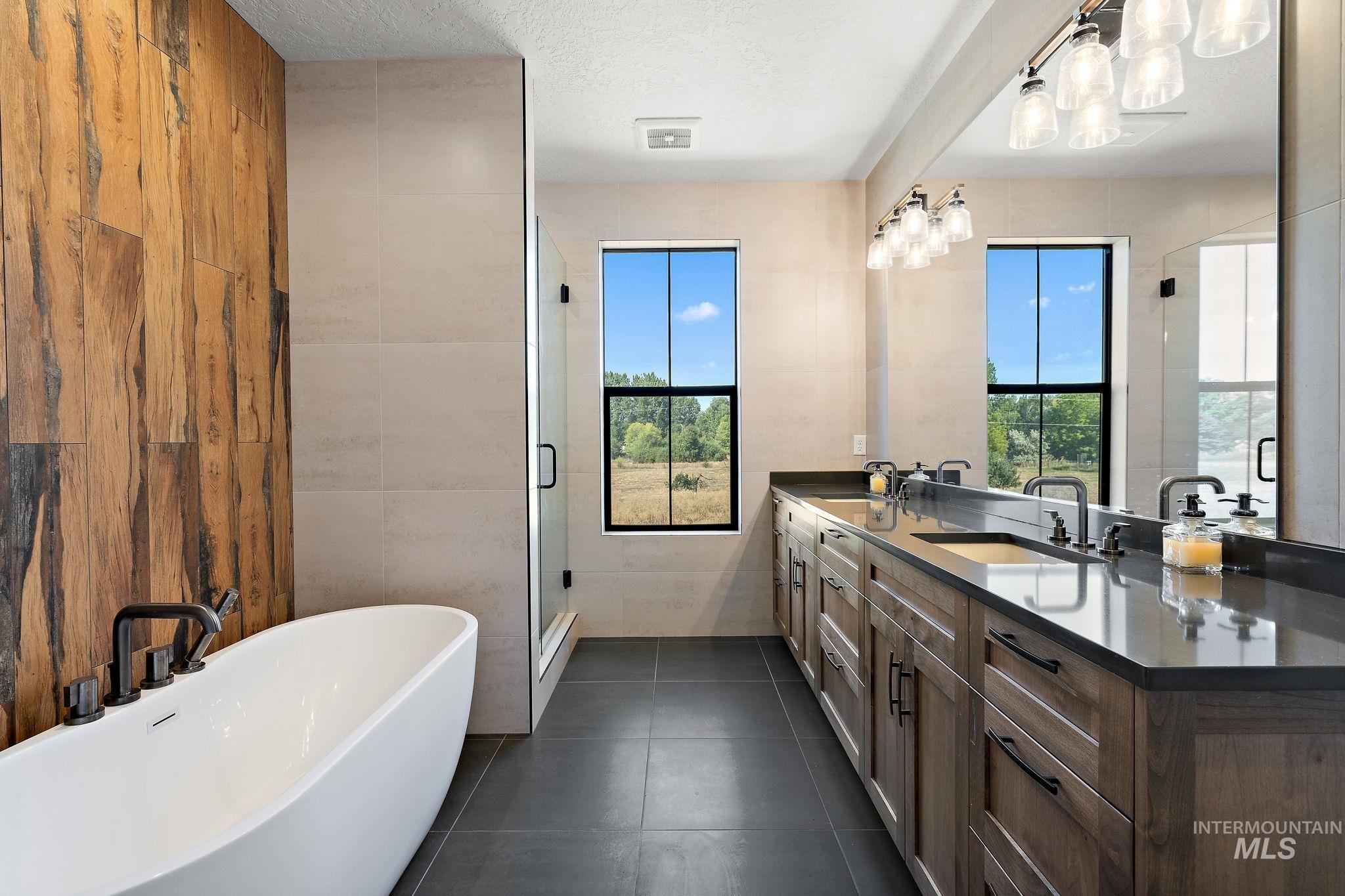 Bathroom with tile walls, double vanity, a soaking tub, a shower stall, and dark tile patterned flooring