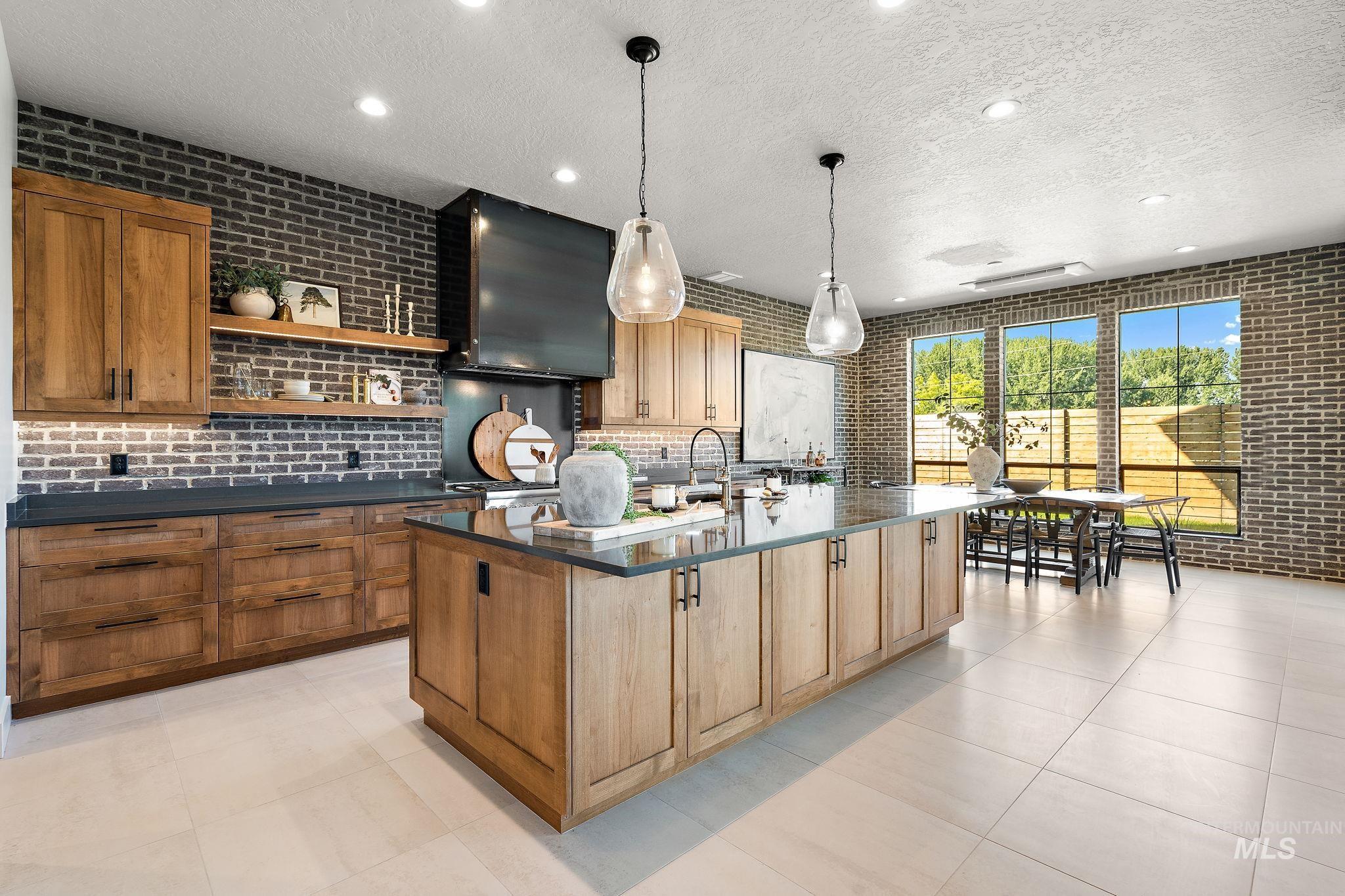 Kitchen featuring a textured ceiling, open shelves, an island with sink, brick wall, and dark stone counters
