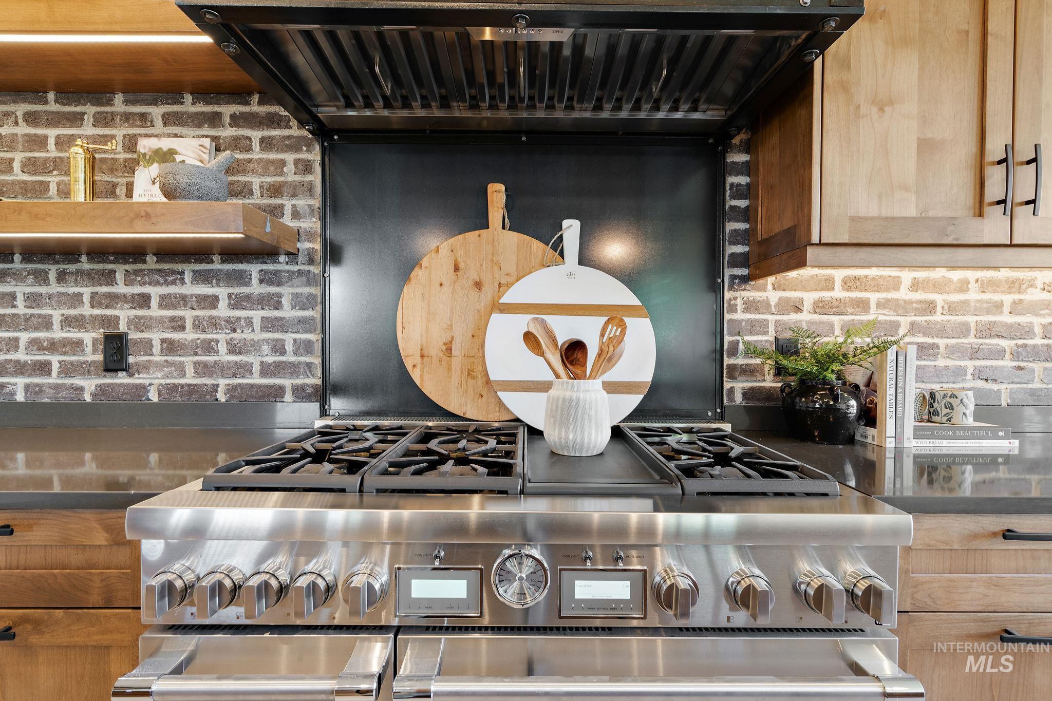 Kitchen view of extractor fan, high end stainless steel range, decorative backsplash, and light brown cabinetry