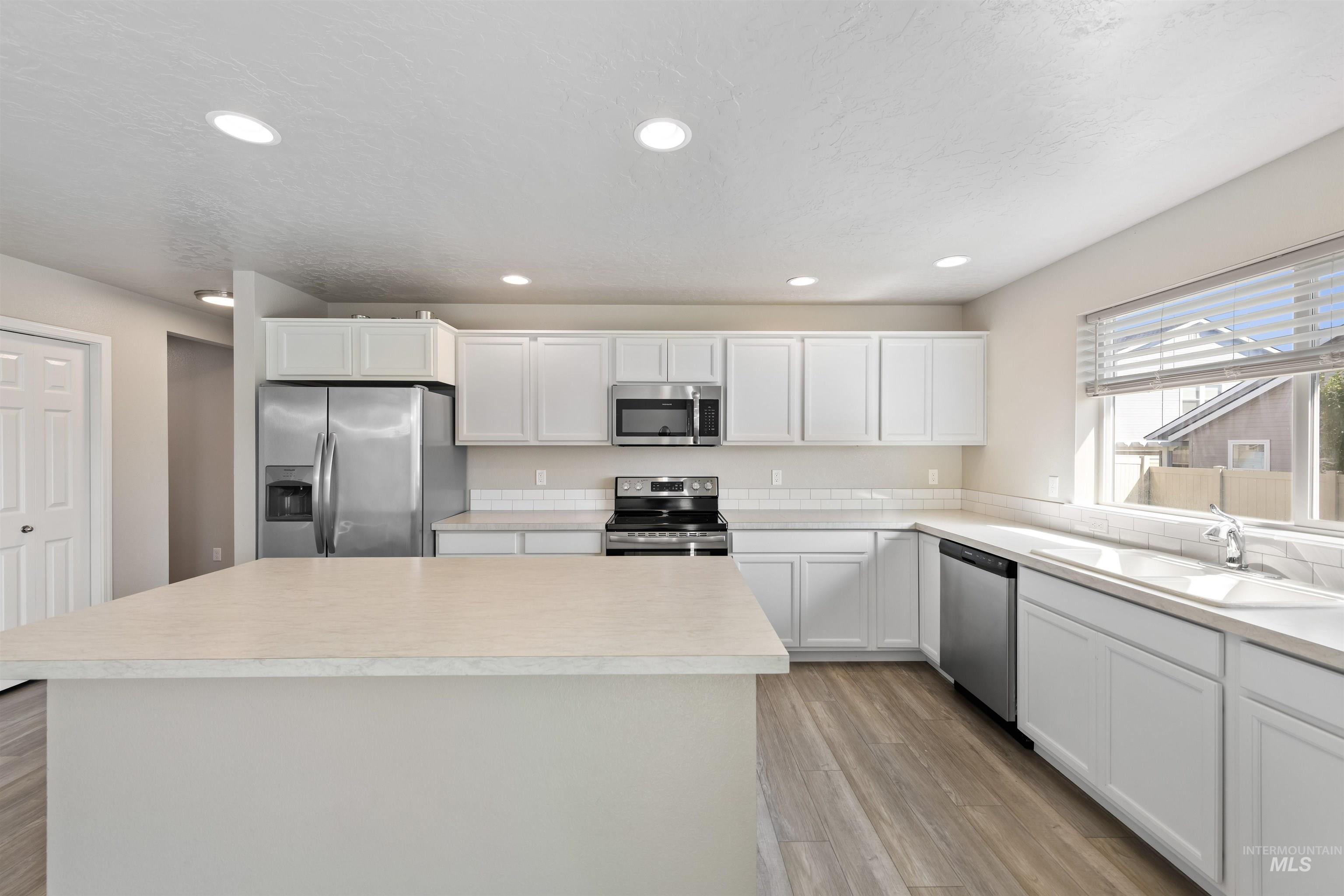 Kitchen with white cabinetry, appliances with stainless steel finishes, light countertops, recessed lighting, and a kitchen island