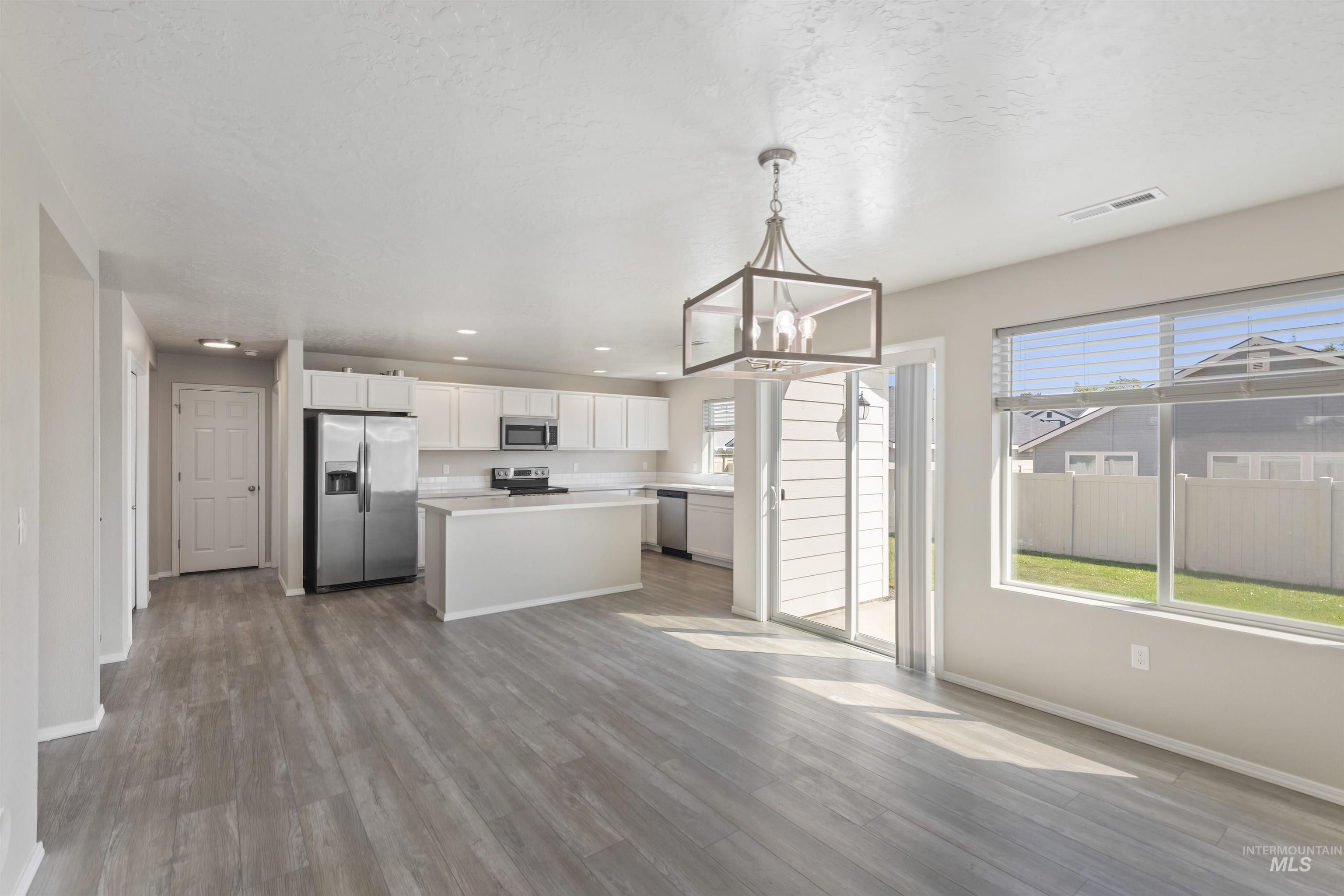Kitchen with white cabinetry, appliances with stainless steel finishes, light countertops, a kitchen island, and light wood-type flooring
