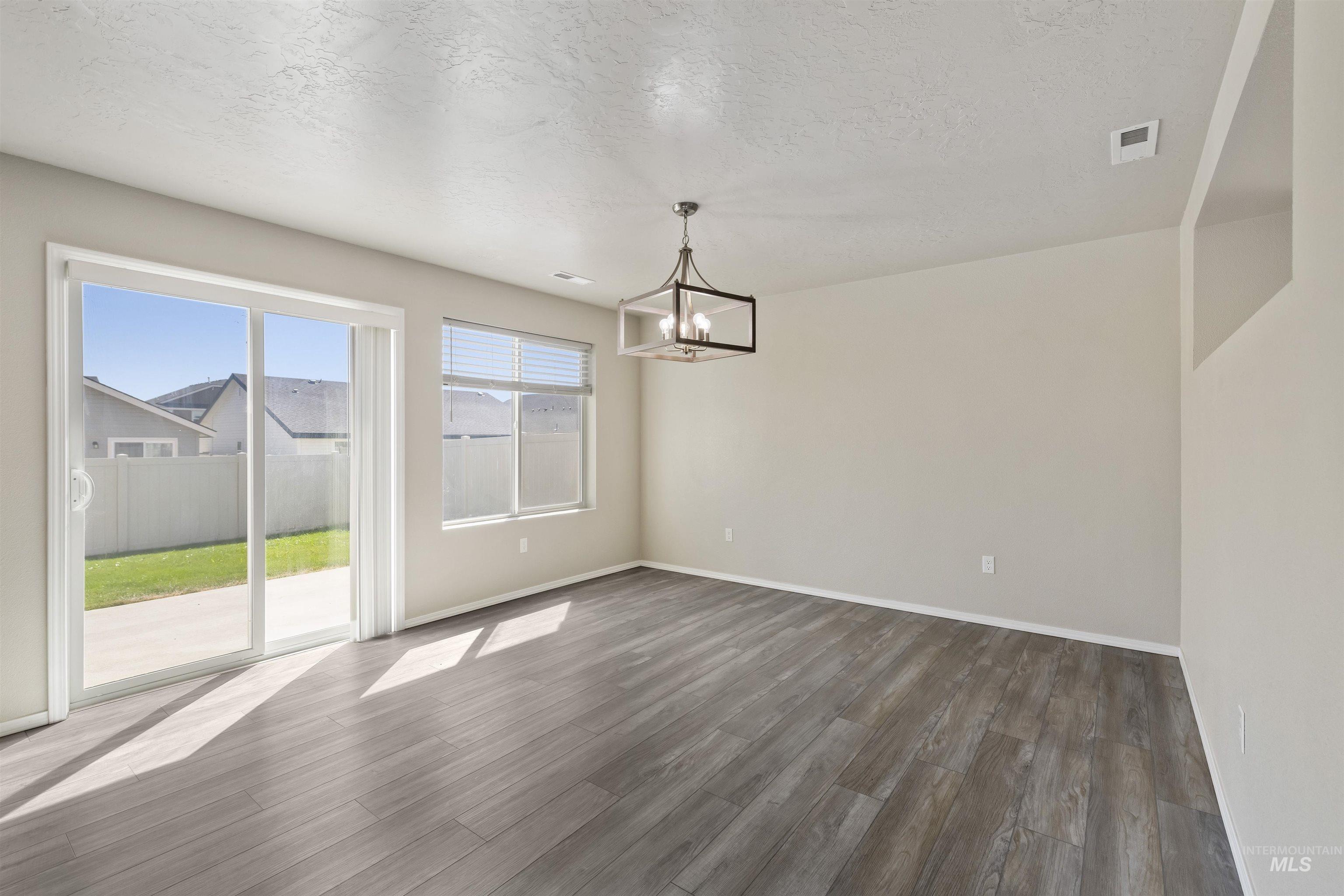 Unfurnished dining area featuring a textured ceiling, dark wood finished floors, and a chandelier