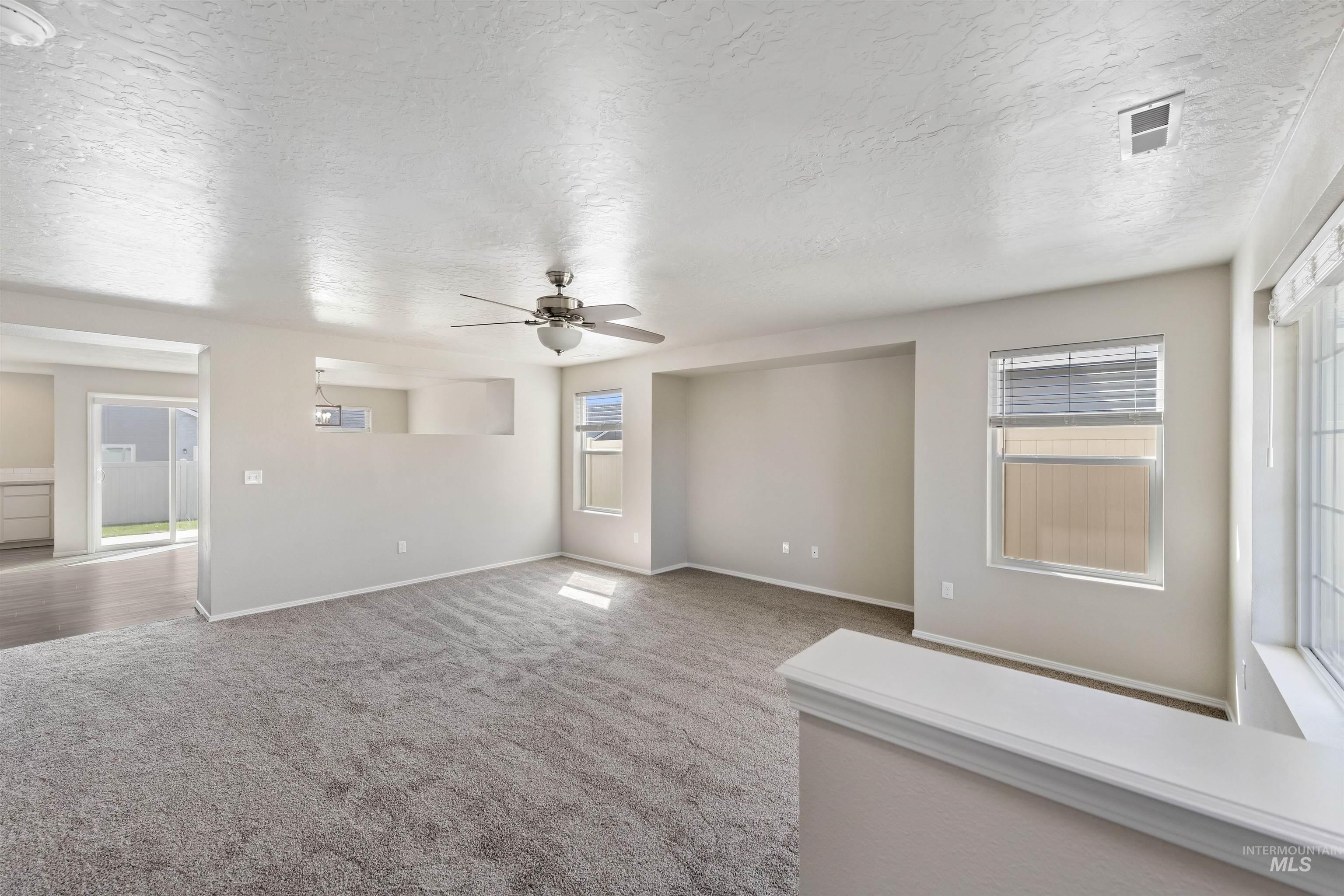 Unfurnished living room with carpet floors, a textured ceiling, and a ceiling fan