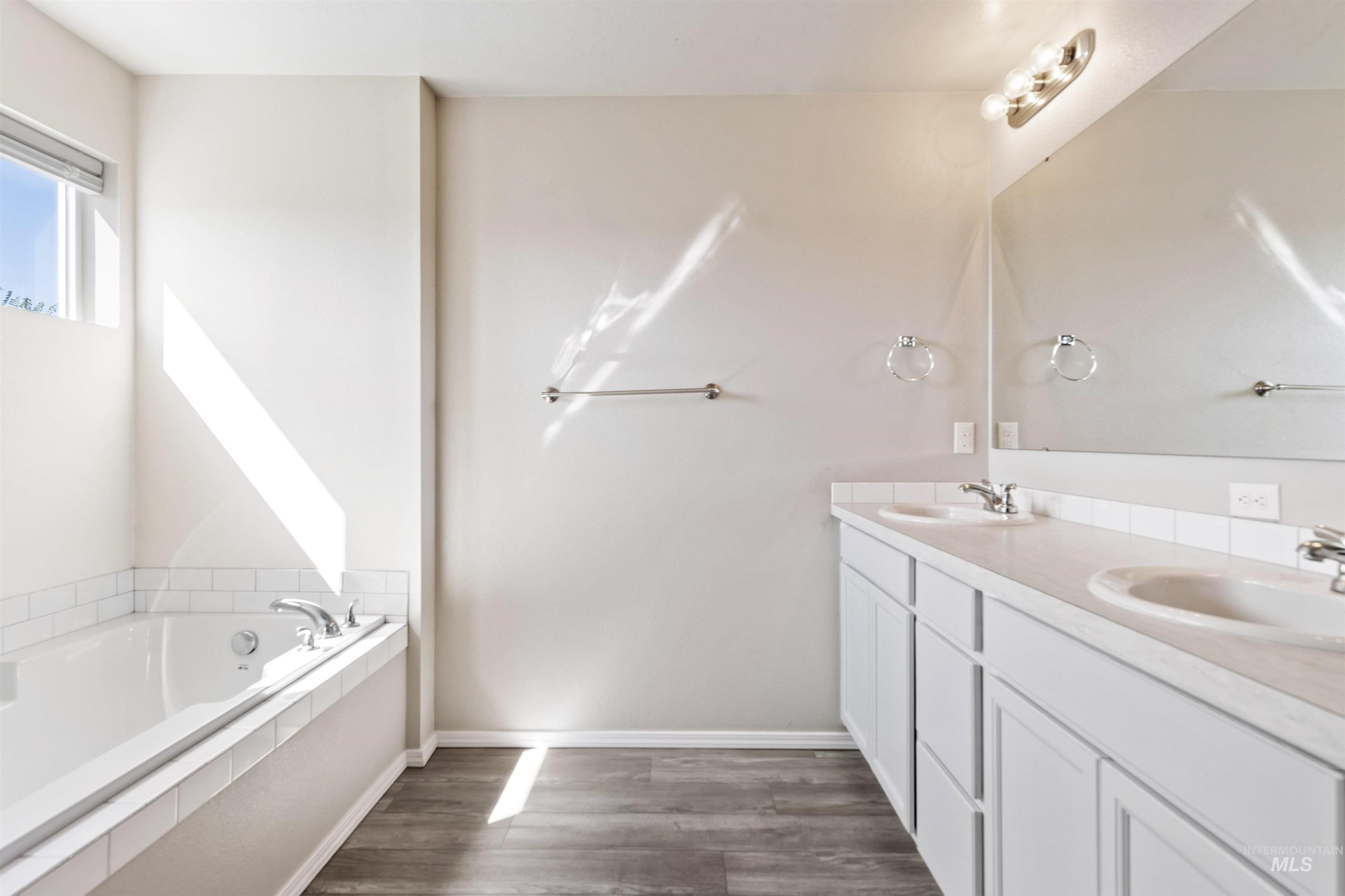Bathroom featuring double vanity, a garden tub, and dark wood-type flooring