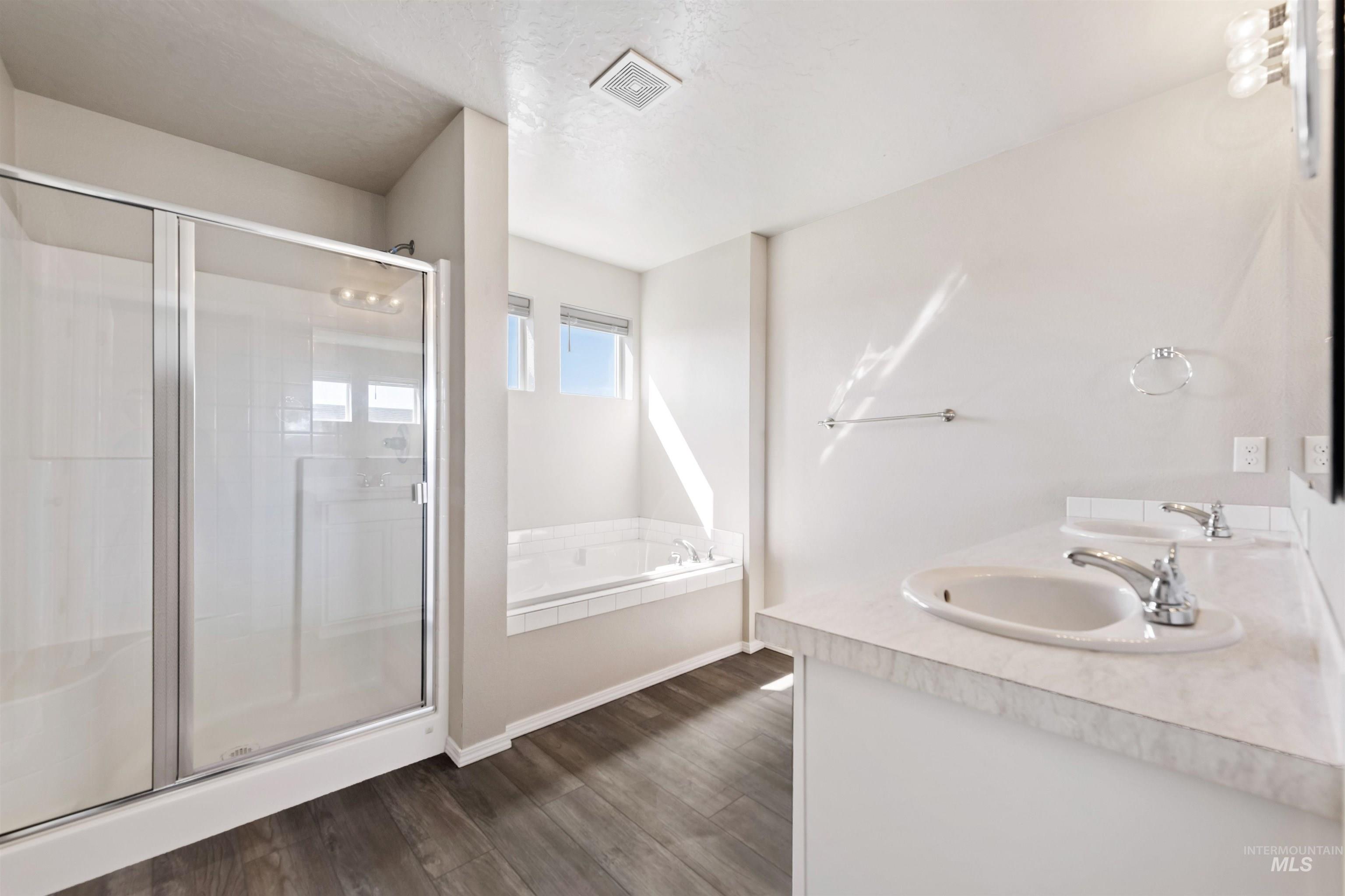 Bathroom with a shower stall, a garden tub, double vanity, dark wood finished floors, and a textured ceiling