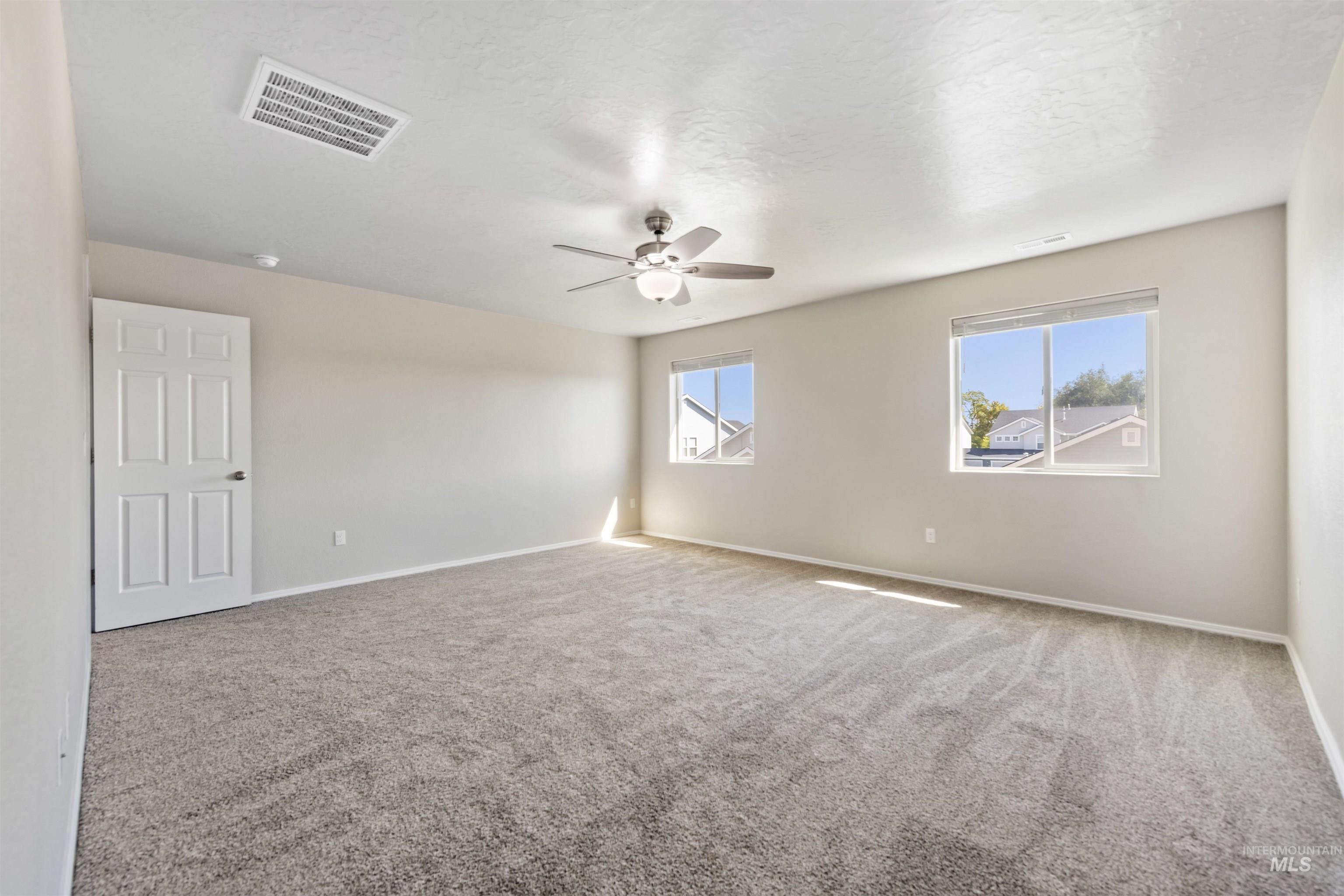 Empty room featuring healthy amount of natural light, carpet, ceiling fan, and a textured ceiling