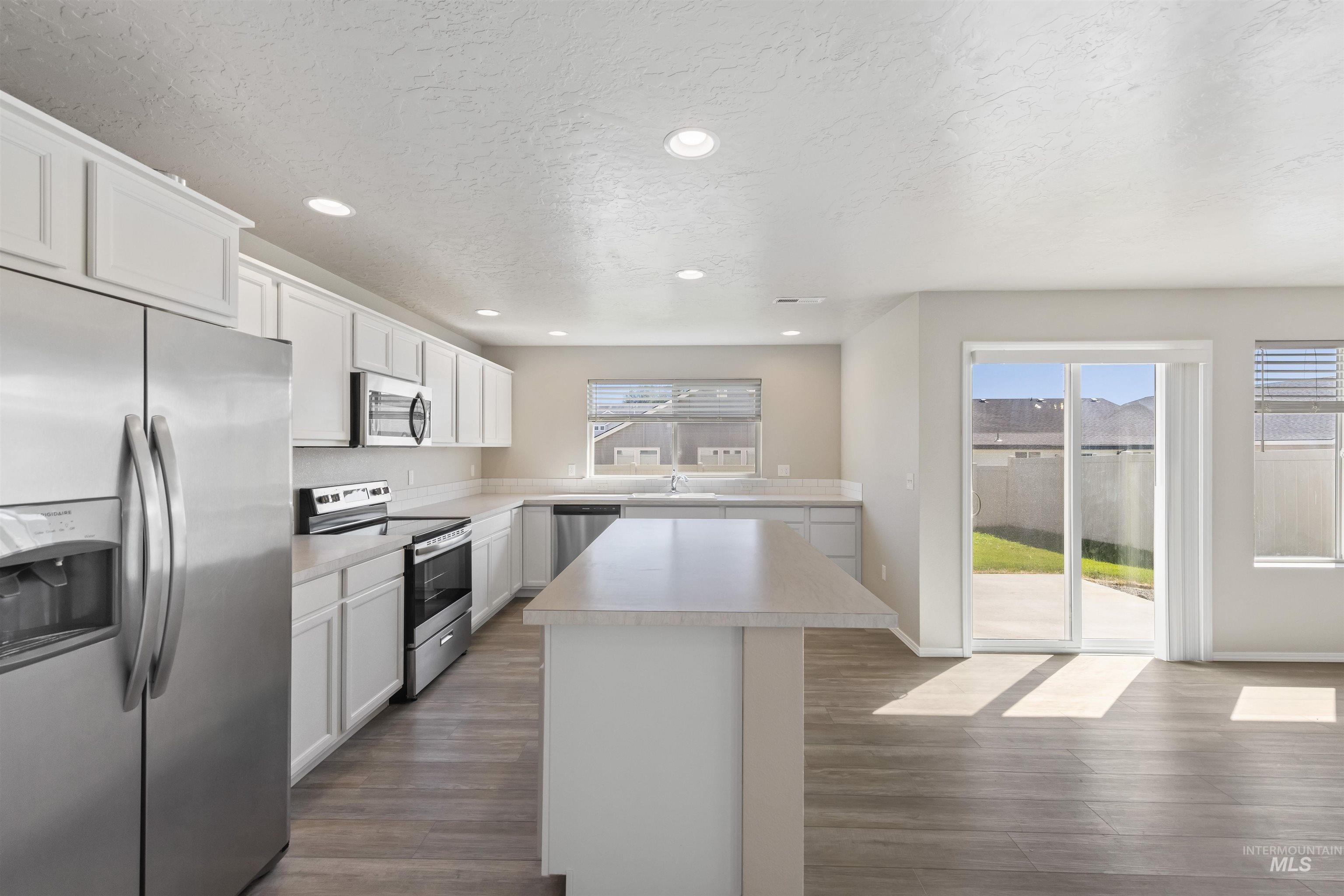 Kitchen with appliances with stainless steel finishes, light countertops, white cabinetry, a center island, and healthy amount of natural light