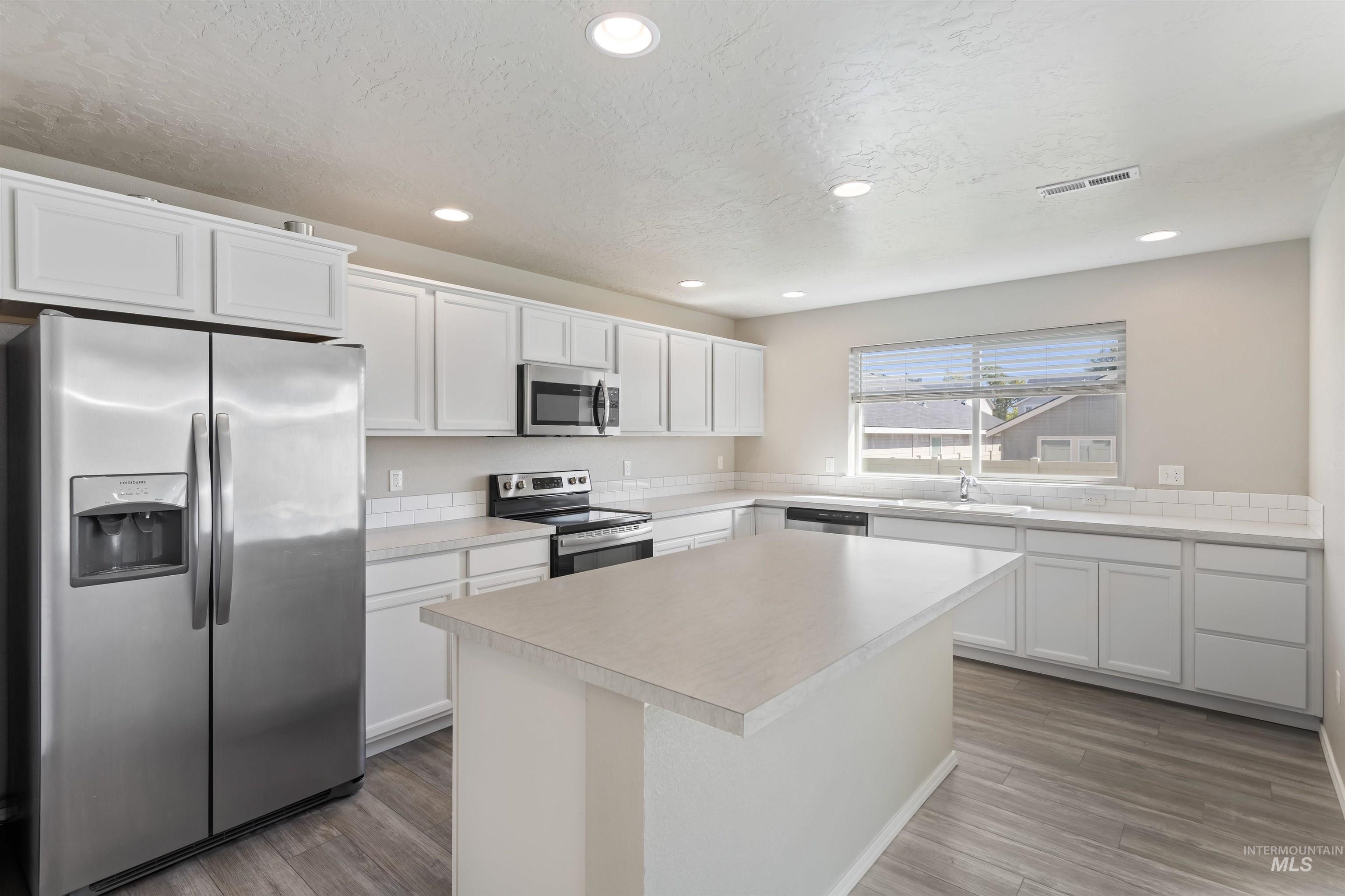 Kitchen featuring appliances with stainless steel finishes, white cabinetry, light countertops, recessed lighting, and a kitchen island