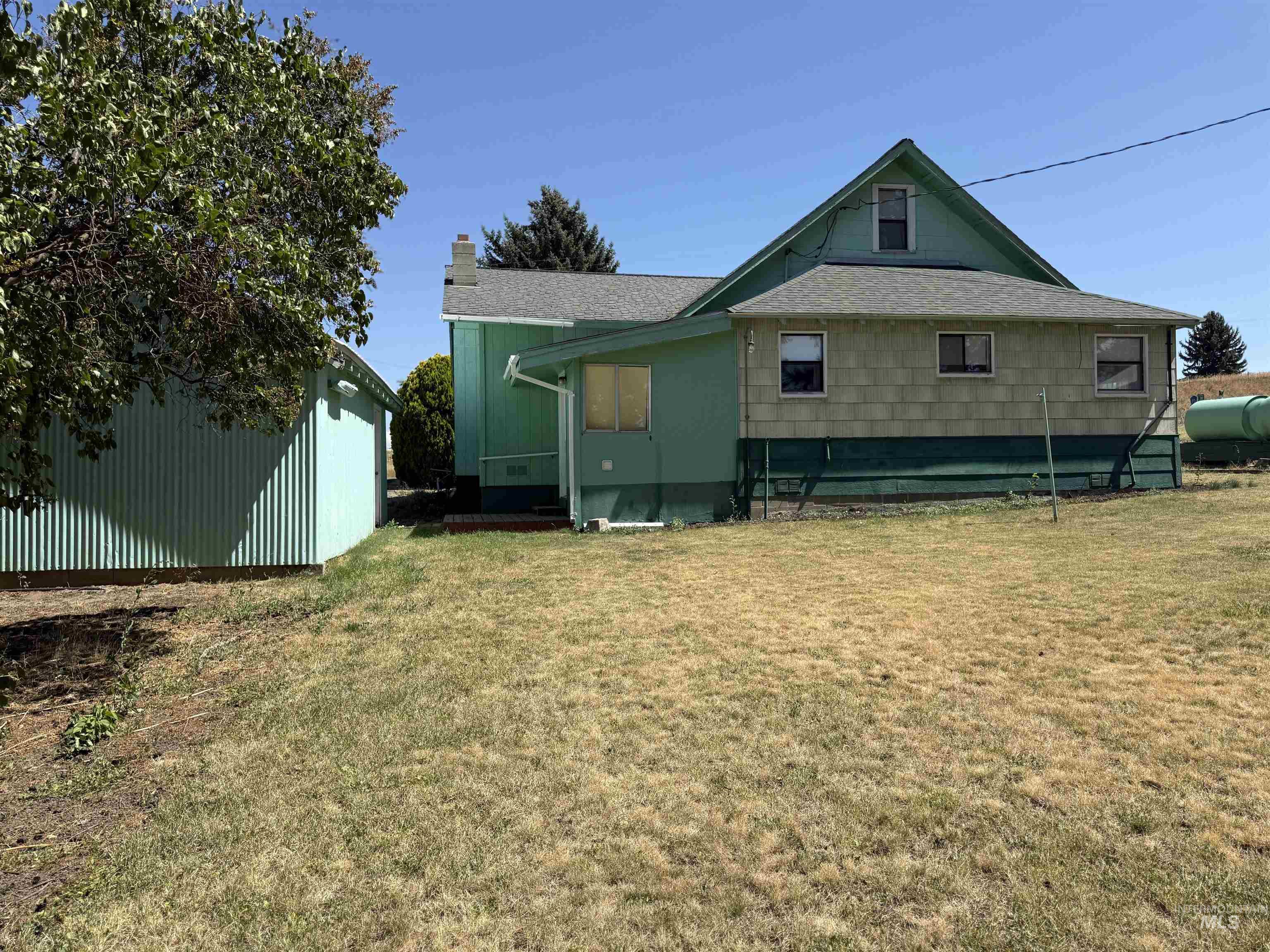 Rear view of house with a lawn, an outbuilding, a chimney, and oil tank