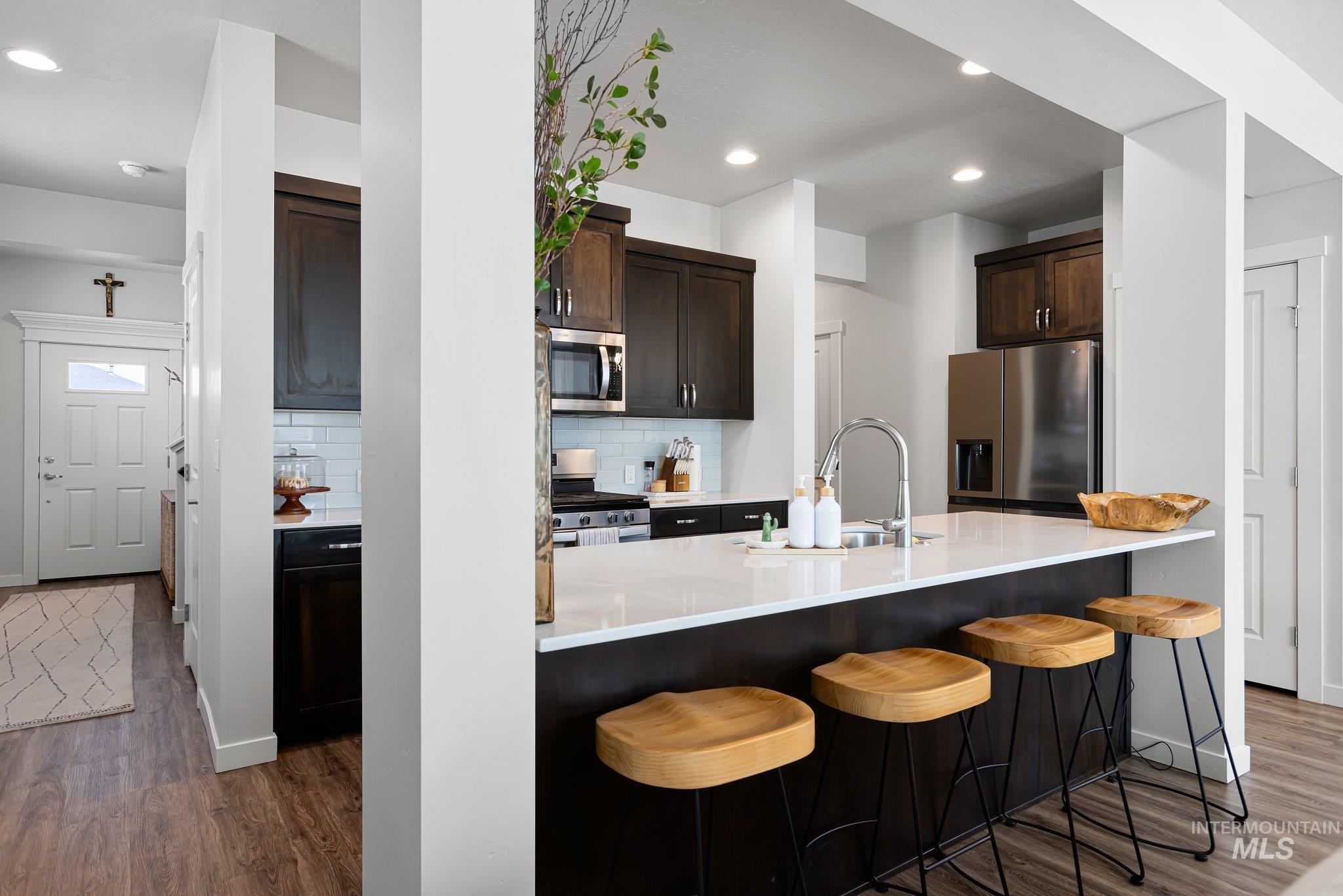 Kitchen with stainless steel appliances, dark wood-style floors, decorative backsplash, dark brown cabinetry, and recessed lighting