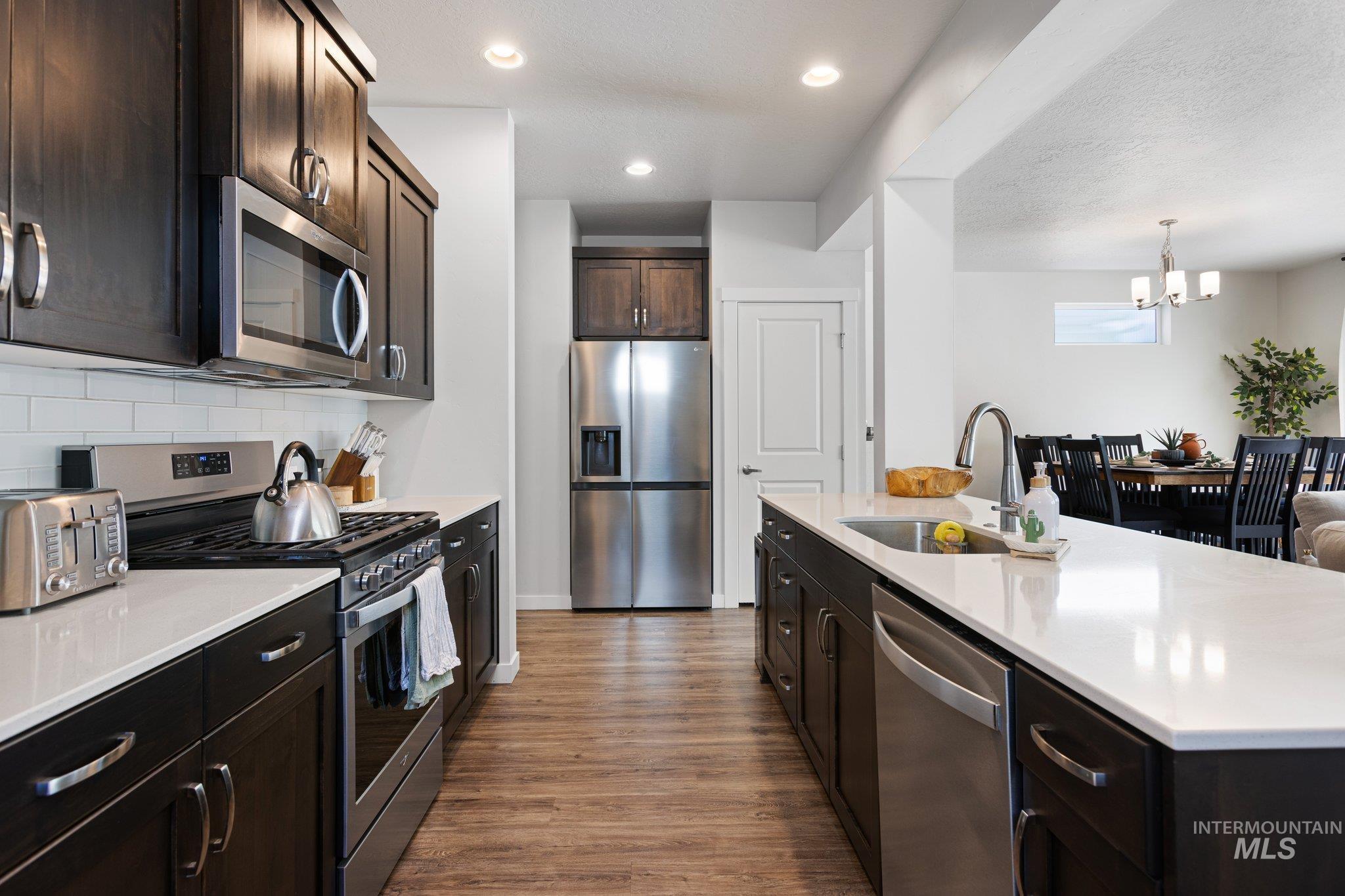 Kitchen featuring dark brown cabinets, appliances with stainless steel finishes, dark wood-style floors, light stone counters, and recessed lighting