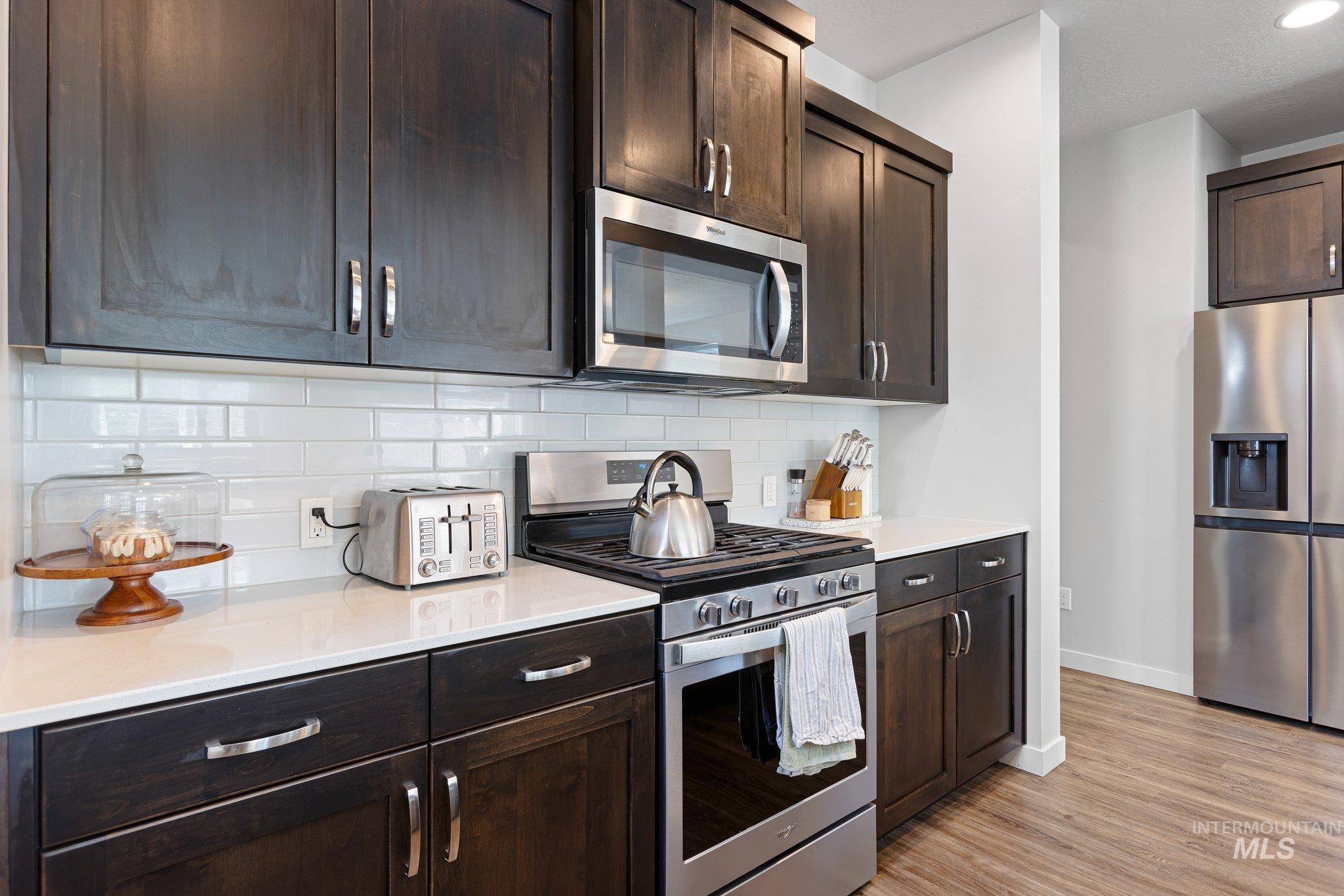 Kitchen with appliances with stainless steel finishes, dark brown cabinetry, light wood finished floors, and decorative backsplash