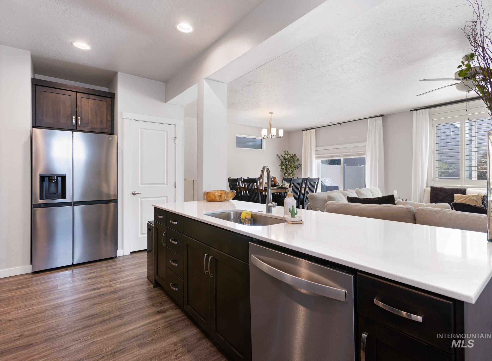 Kitchen featuring appliances with stainless steel finishes, dark brown cabinets, open floor plan, a textured ceiling, and dark wood finished floors