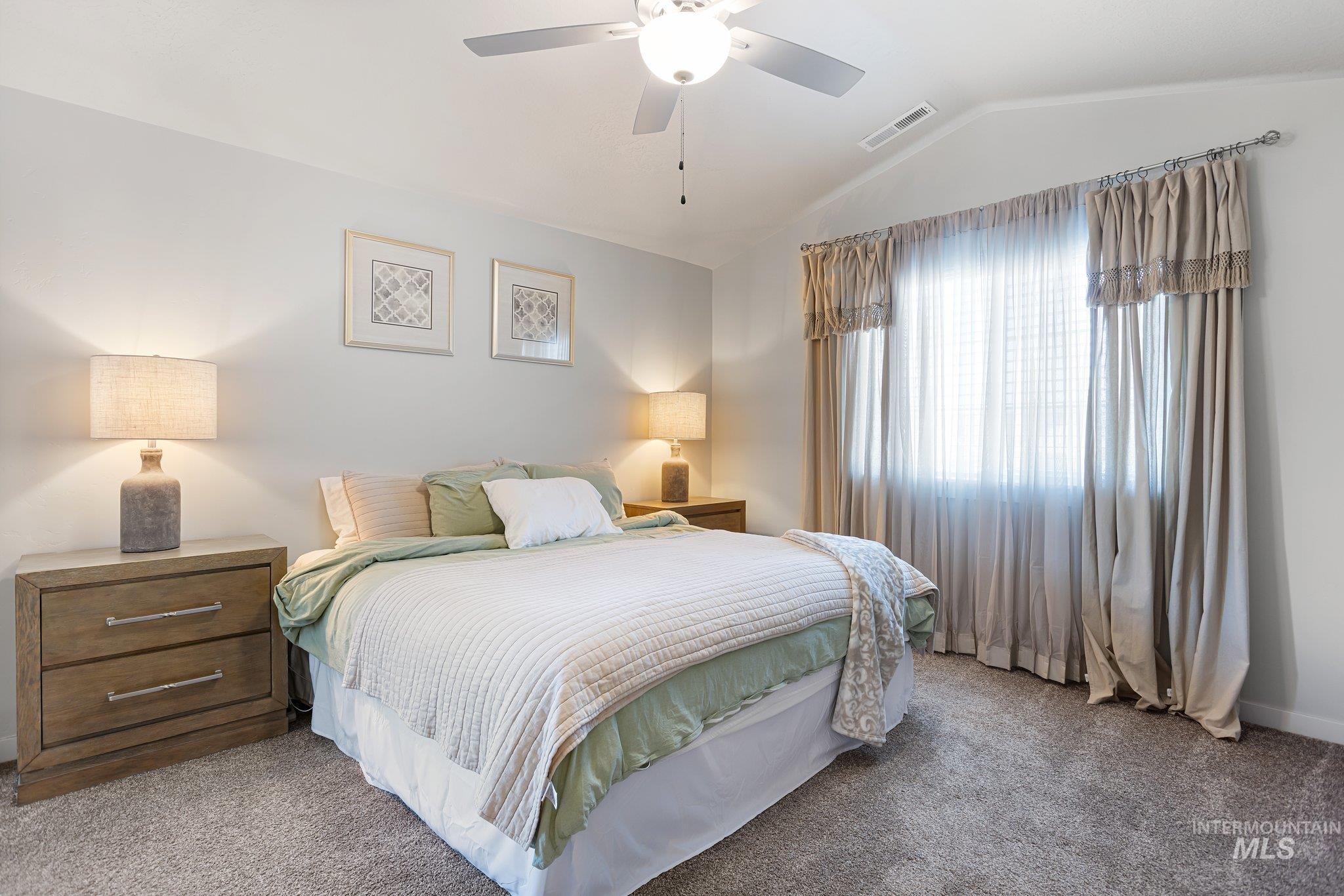 Carpeted bedroom featuring vaulted ceiling and a ceiling fan