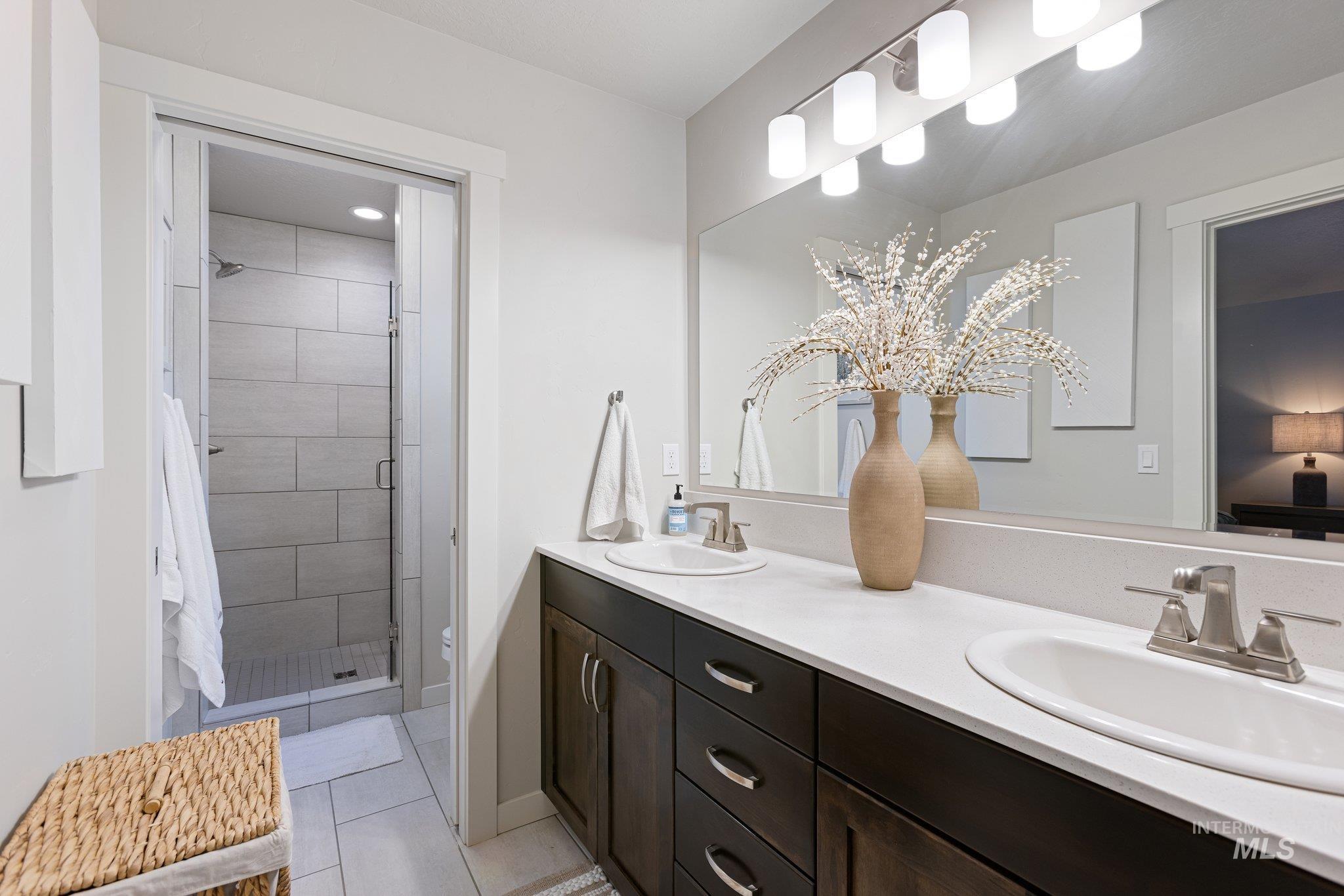 Full bathroom with double vanity, a stall shower, and light tile patterned flooring