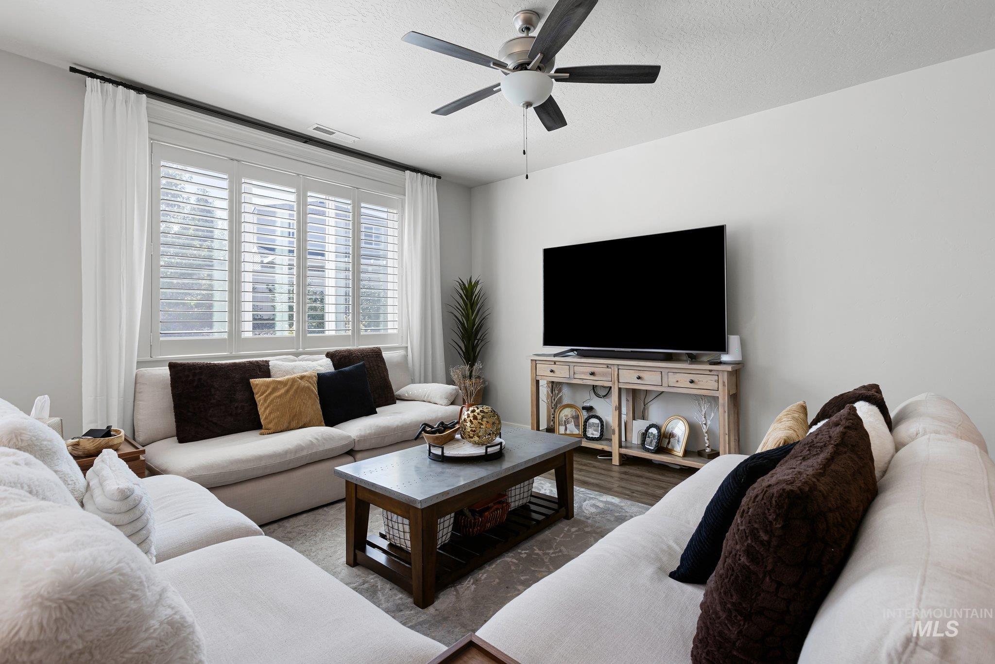 Living room with a textured ceiling, wood finished floors, and a ceiling fan