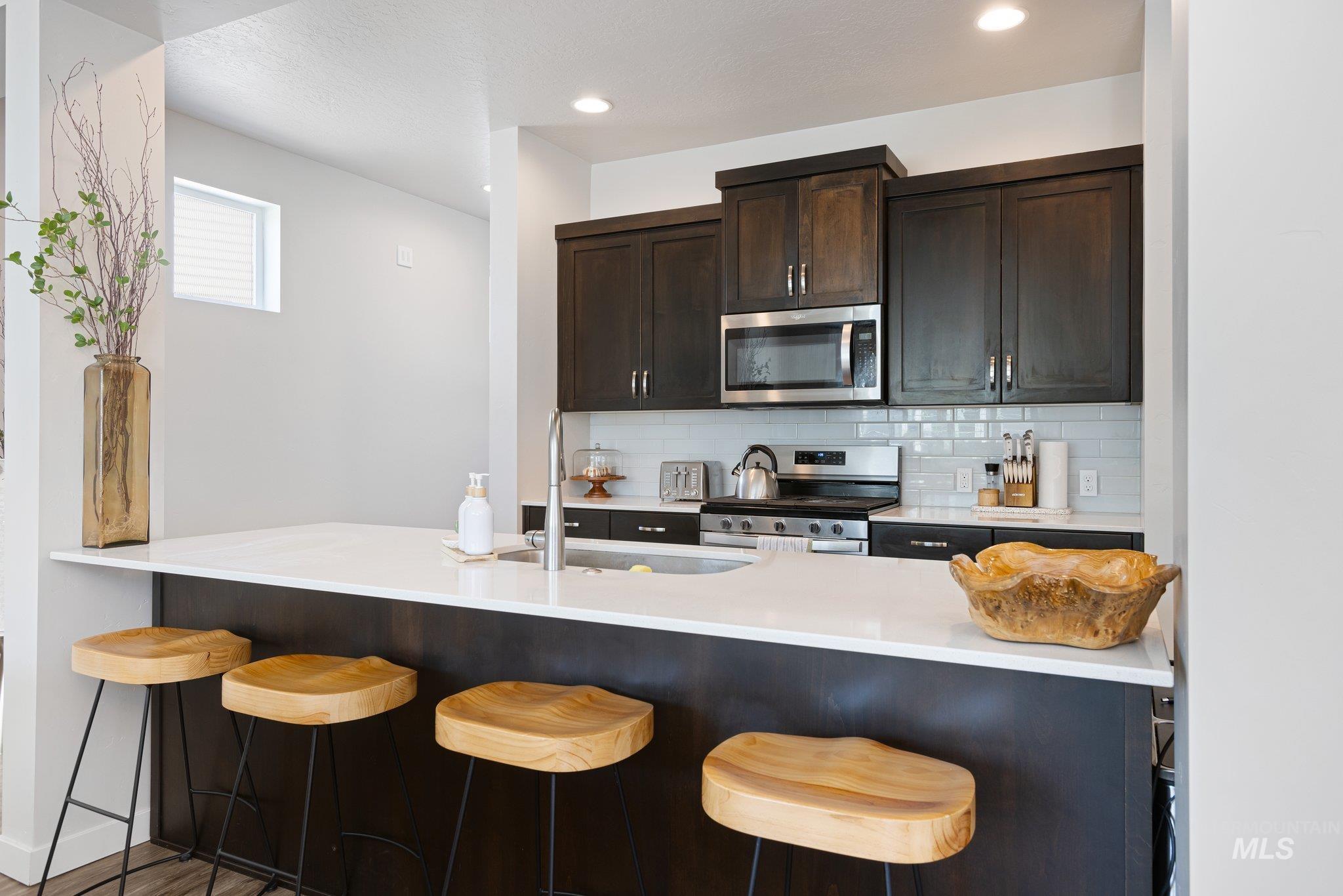 Kitchen featuring dark brown cabinets, tasteful backsplash, stainless steel appliances, a kitchen breakfast bar, and recessed lighting