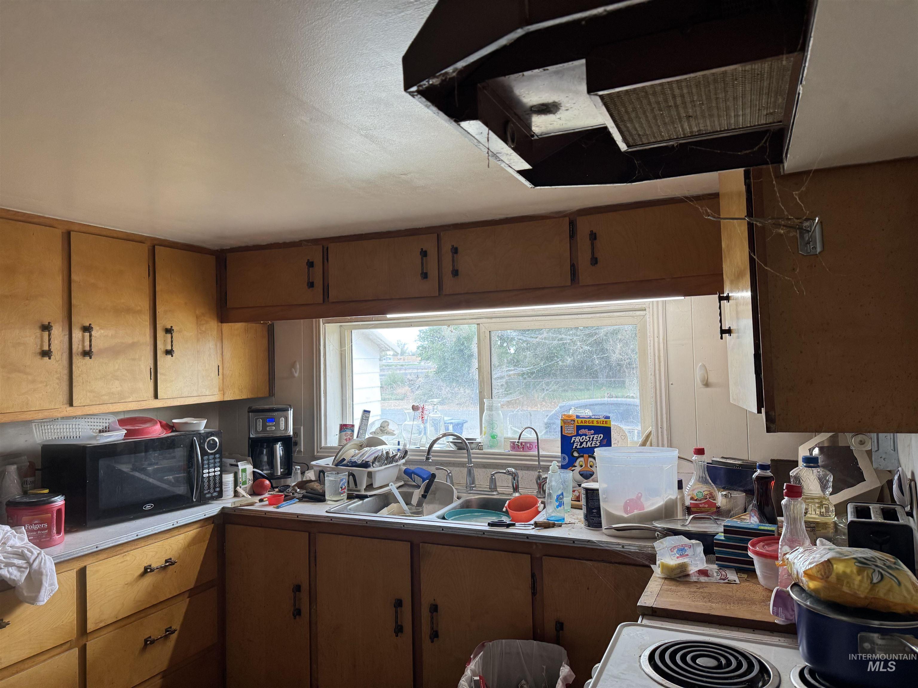 Kitchen featuring extractor fan, light countertops, brown cabinets, black microwave, and white electric range