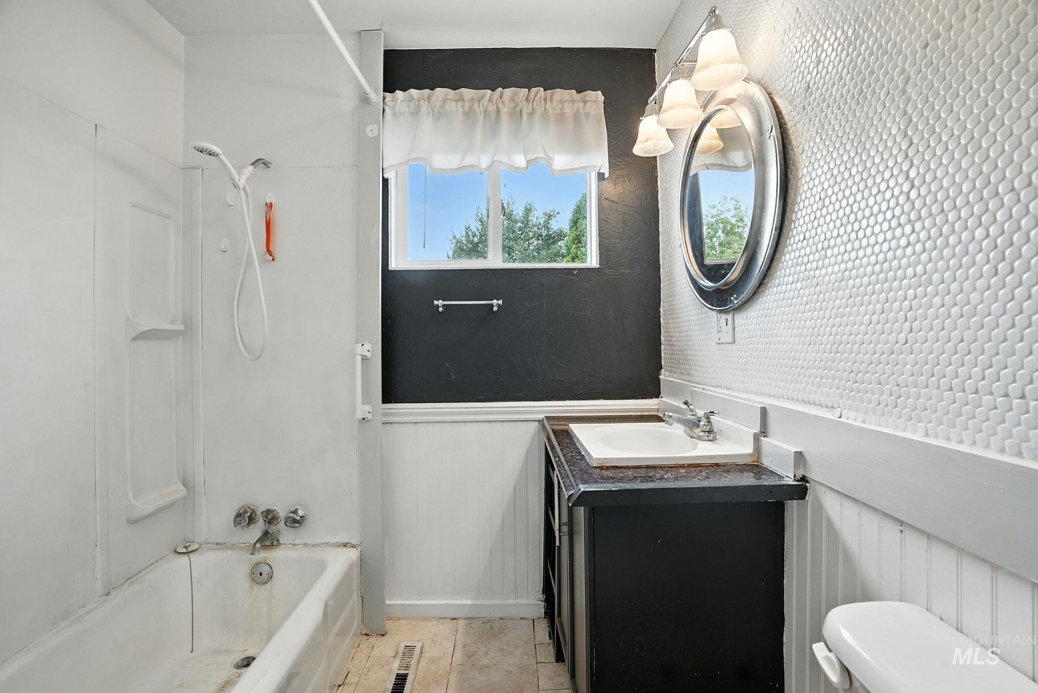 Bathroom featuring shower / tub combination, vanity, light tile patterned floors, and a wainscoted wall