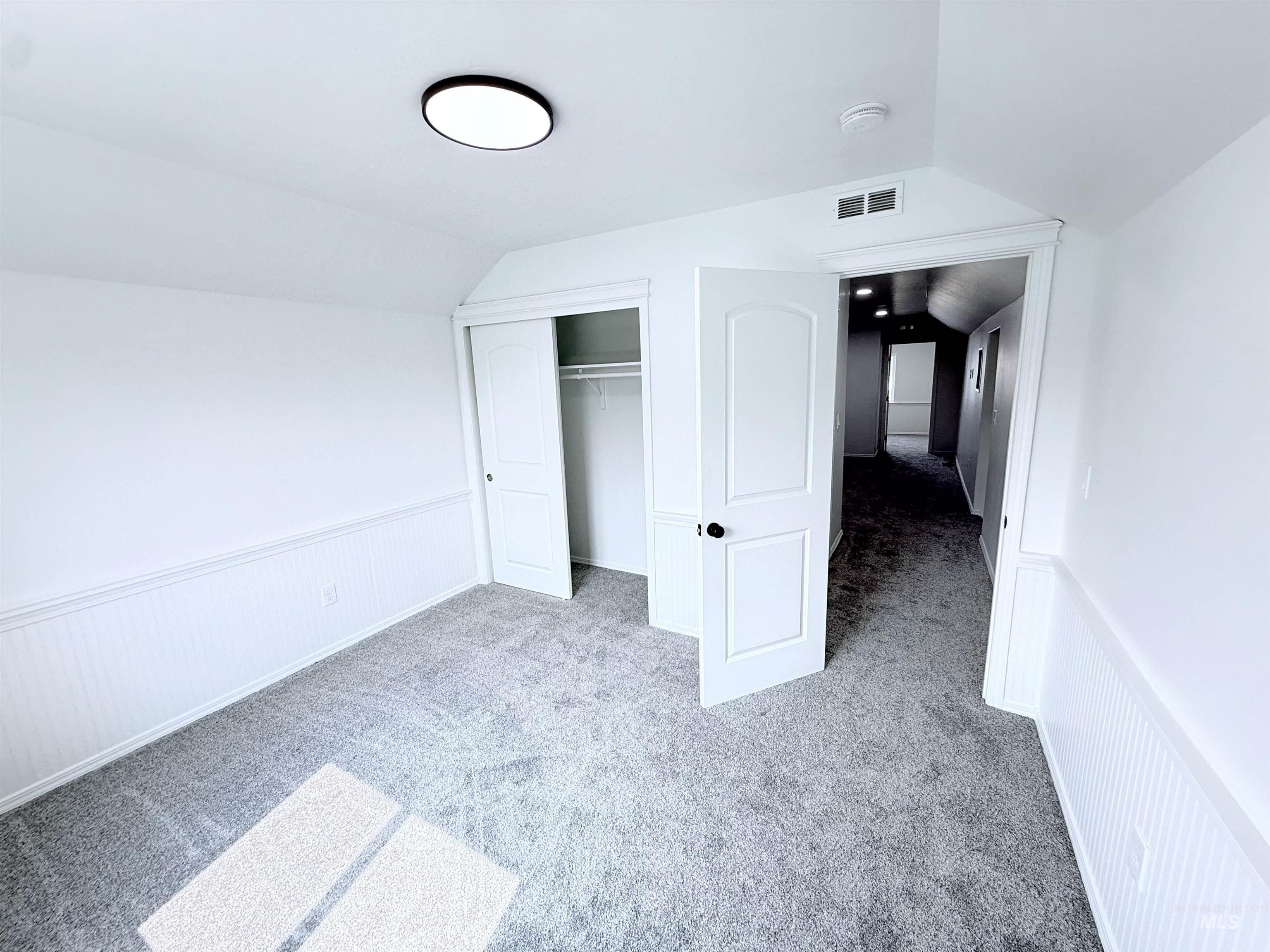 Unfurnished bedroom featuring light colored carpet, lofted ceiling, a closet, and a wainscoted wall