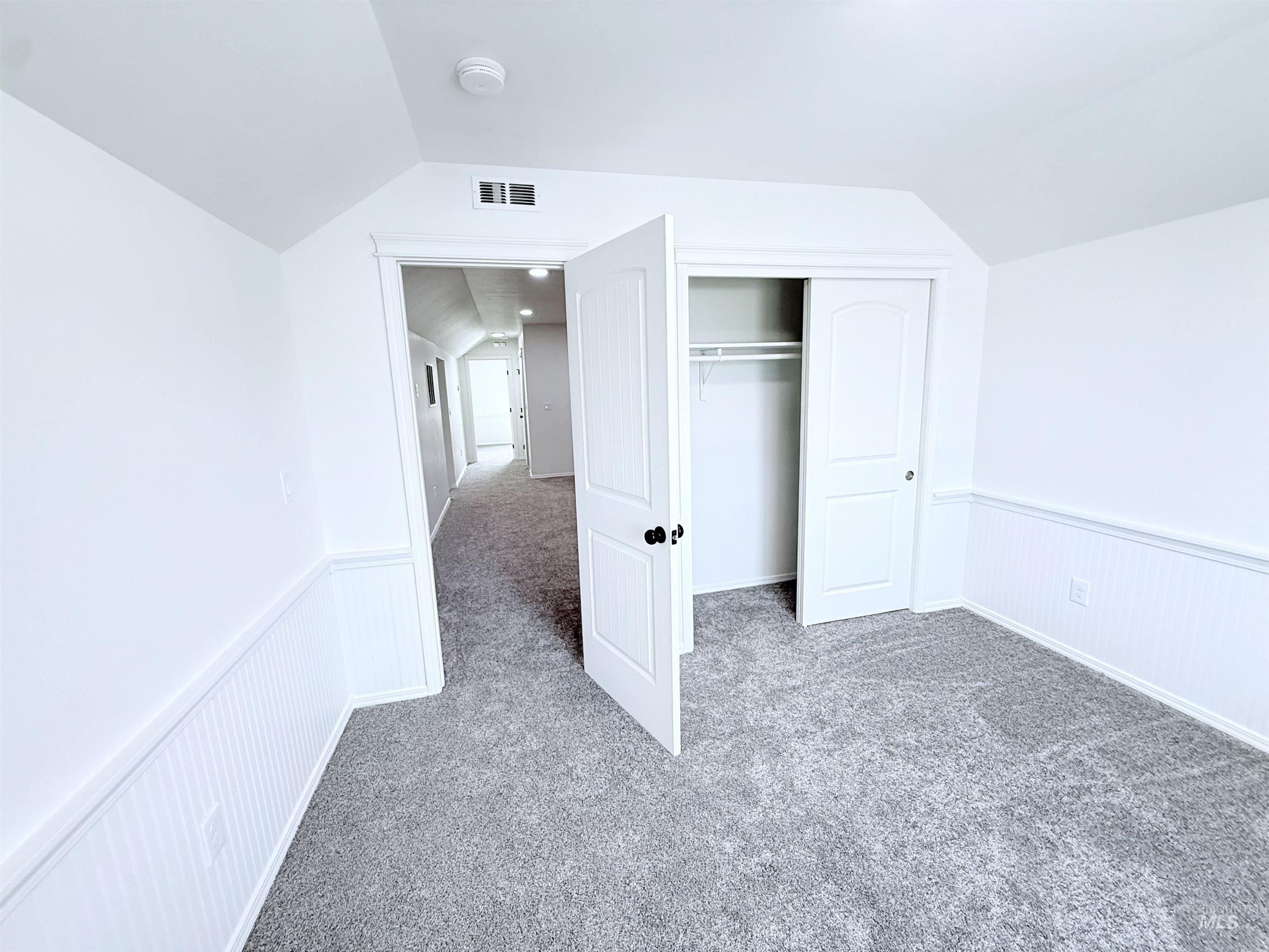 Unfurnished bedroom with carpet floors, lofted ceiling, a closet, and a wainscoted wall