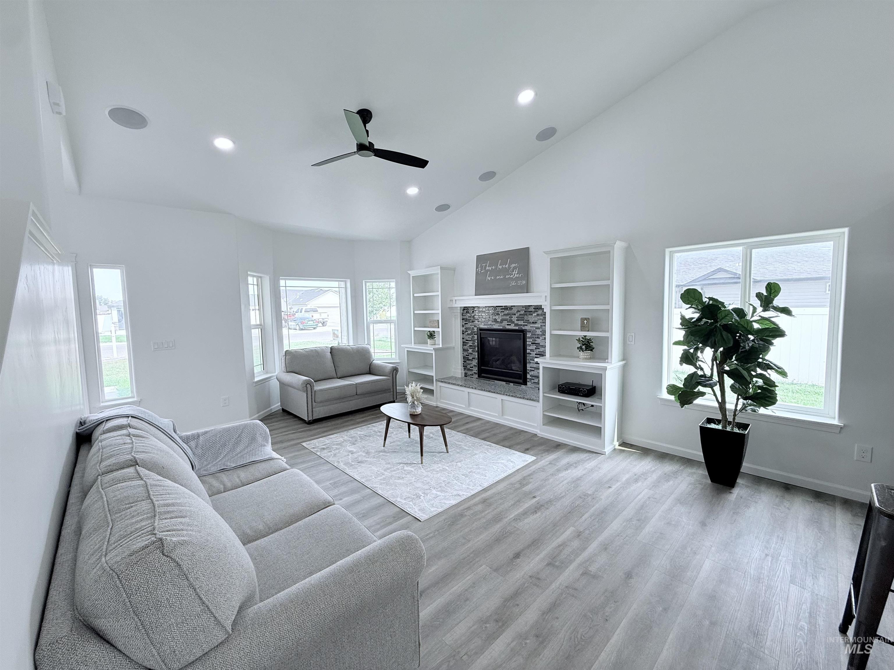 Living area featuring recessed lighting, high vaulted ceiling, a glass covered fireplace, light wood-style floors, and a ceiling fan
