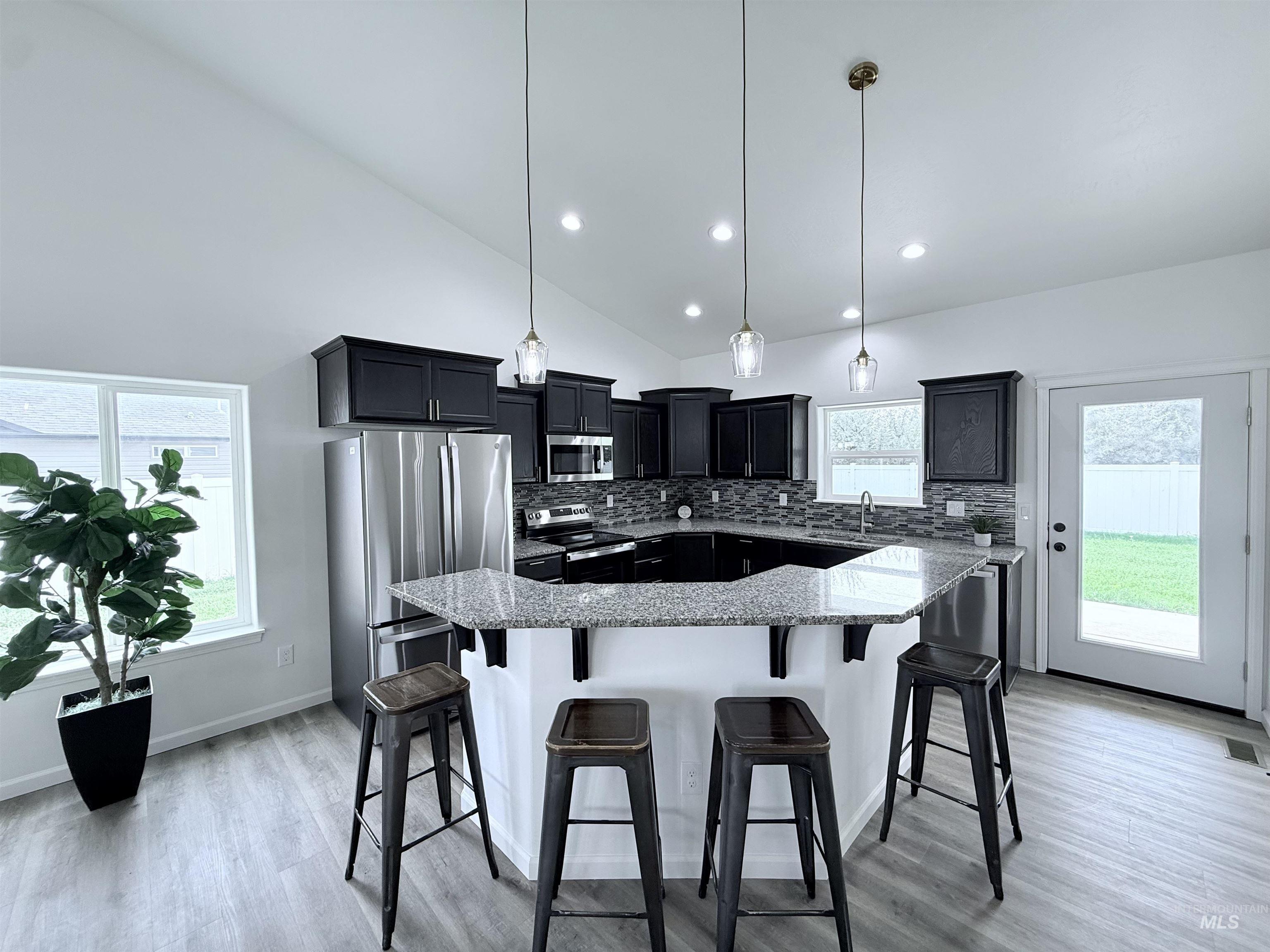 Kitchen with tasteful backsplash, a breakfast bar area, appliances with stainless steel finishes, dark cabinetry, and light stone counters