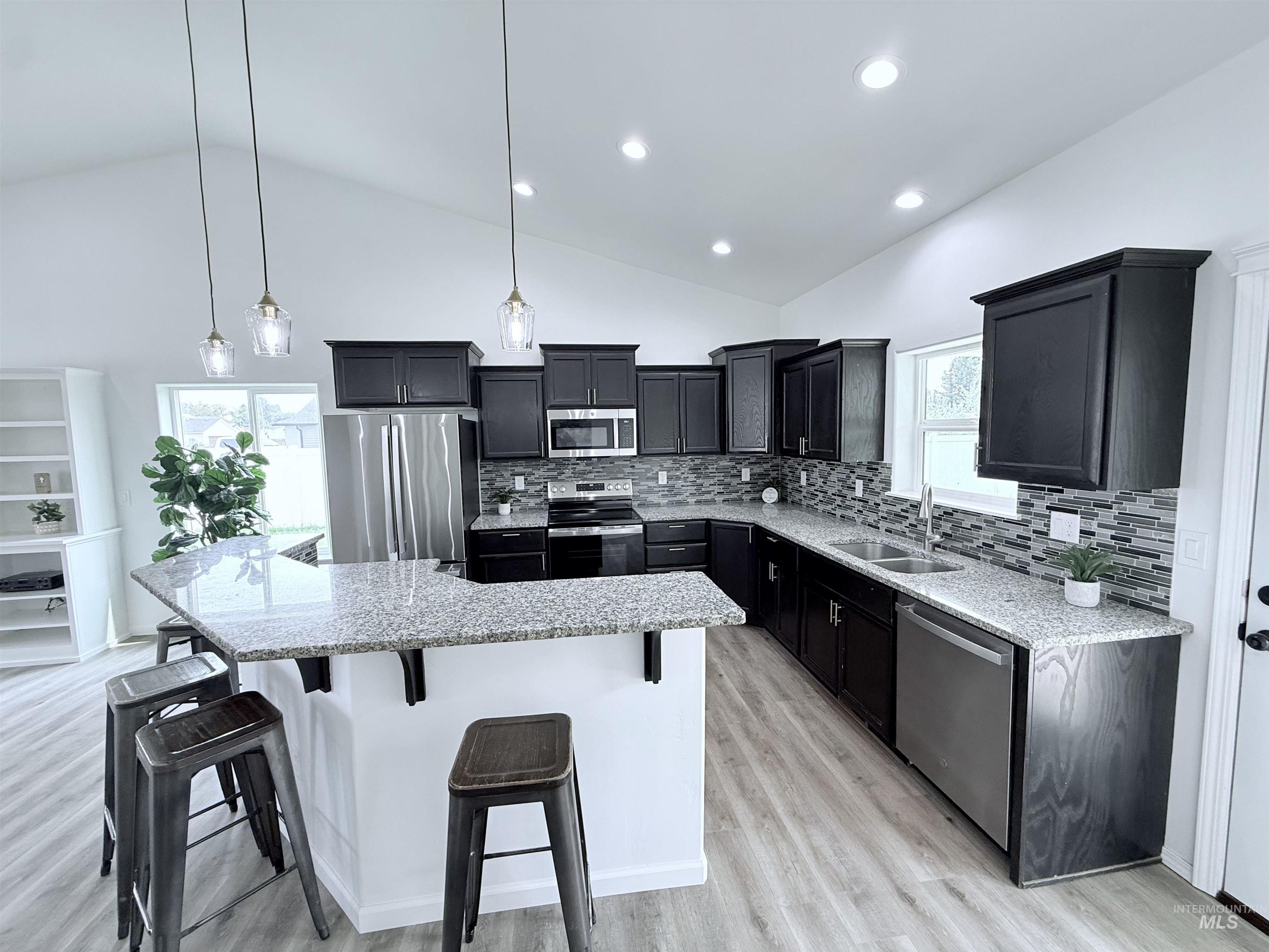 Kitchen with a breakfast bar, stainless steel appliances, light stone counters, light wood-type flooring, and backsplash
